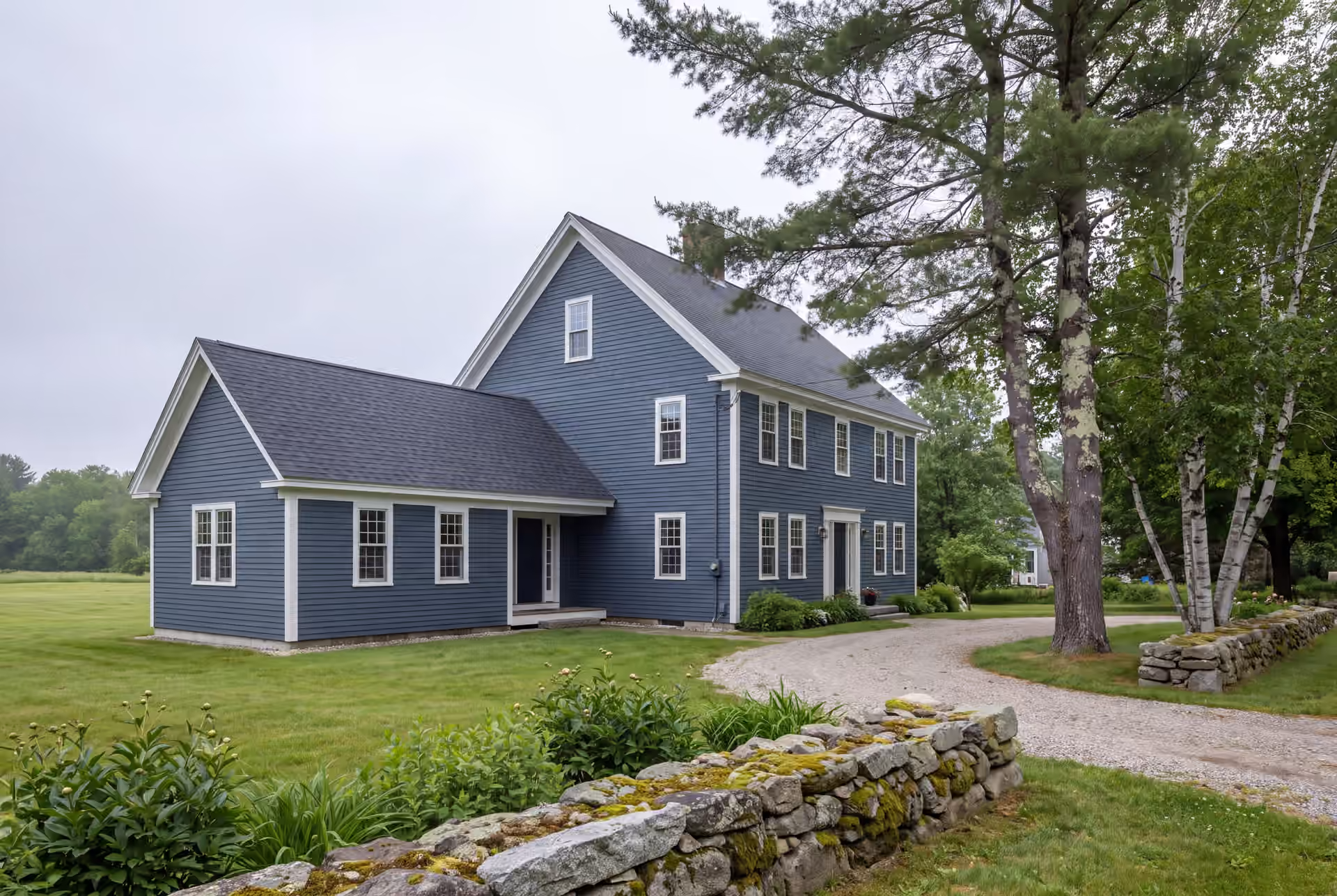home addition builder: illustrative scene, A blue farmhouse with a new addition, seen from a three-quarter exterior view, surrounded by green lawn, trees, and a stone wall