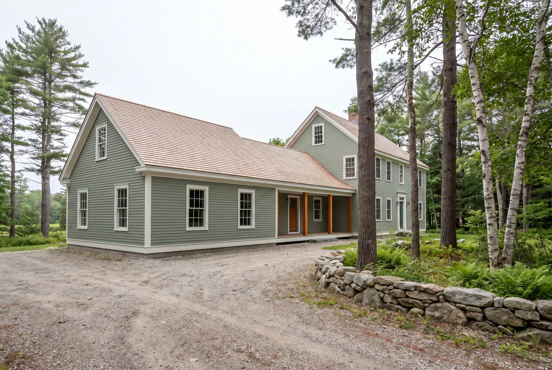 Illustration: A sage green clapboard house with a new single-story addition, light brown shingle roofs, and white trim, viewed from a three-quarter exterior perspective with a gravel driveway and surrounding trees