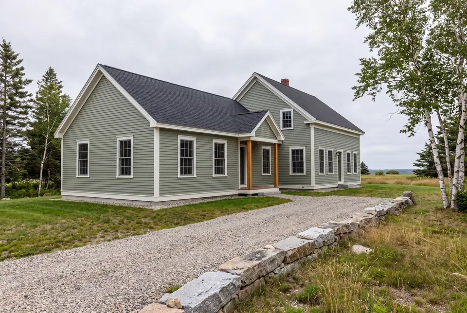 home addition builder in Buxton, ME: illustrative scene, A sage green farmhouse with a new addition, gravel driveway, and stone wall