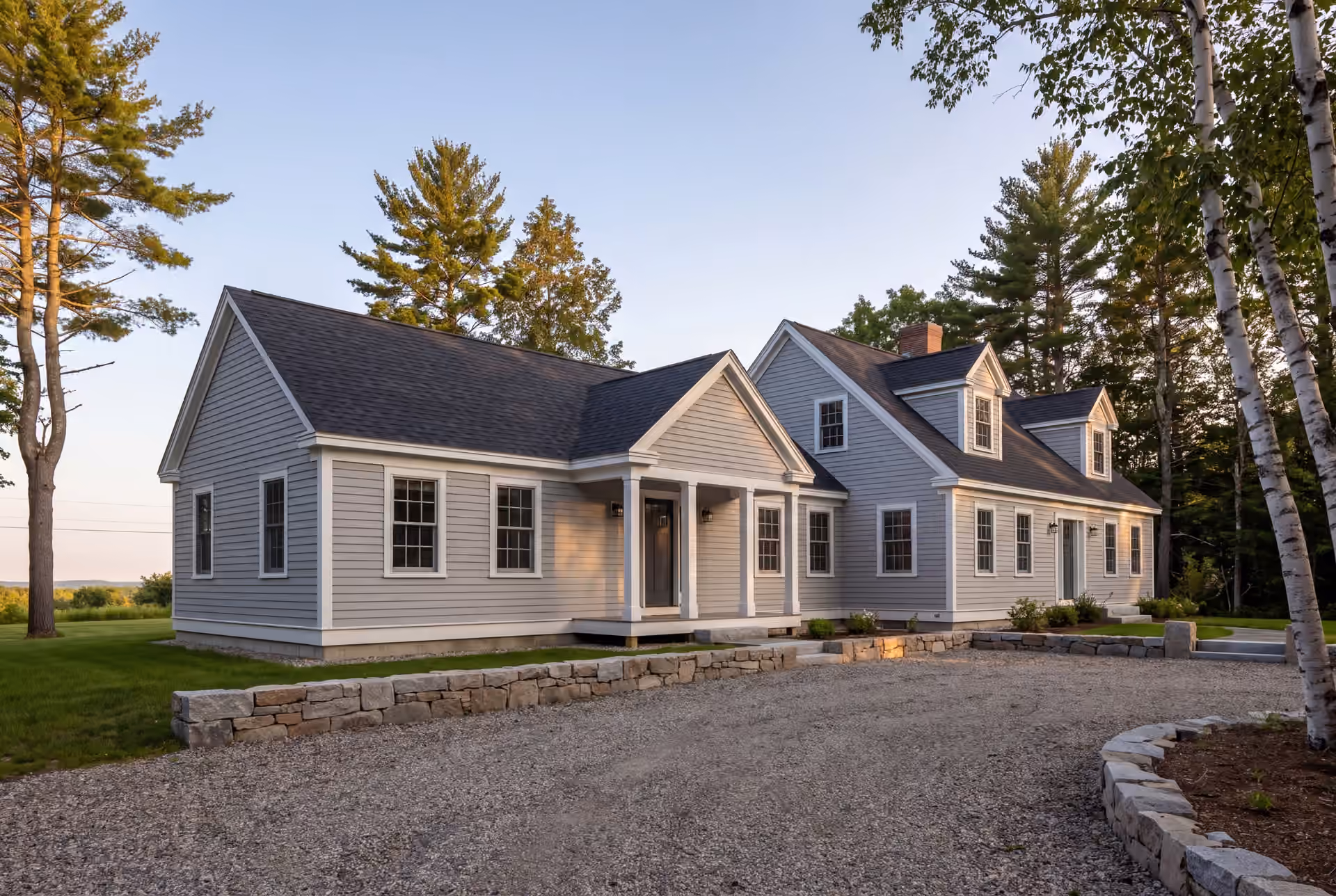 home addition builder in Cape Elizabeth, ME: illustrative scene, A light gray clapboard house with a new single-story addition, featuring a gravel driveway and stone walls in the foreground, and trees in the background