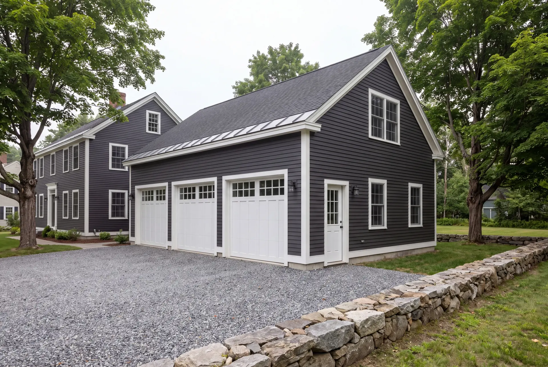 Illustration: A newly built, dark charcoal three-car garage with white doors and trim, next to a matching house, with a gravel driveway and a stone wall