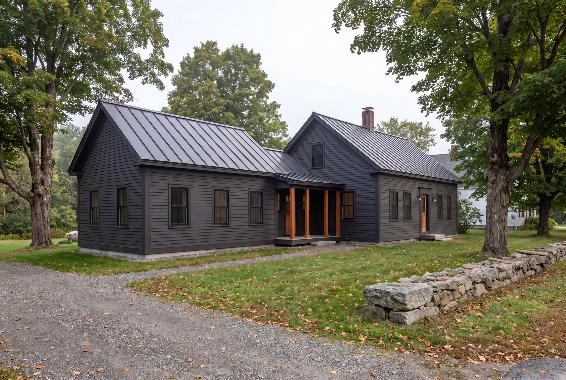 Illustration: A dark charcoal farmhouse with a new addition, featuring a metal roof and natural wood porch posts, surrounded by a lawn, gravel driveway, and stone wall under an overcast sky