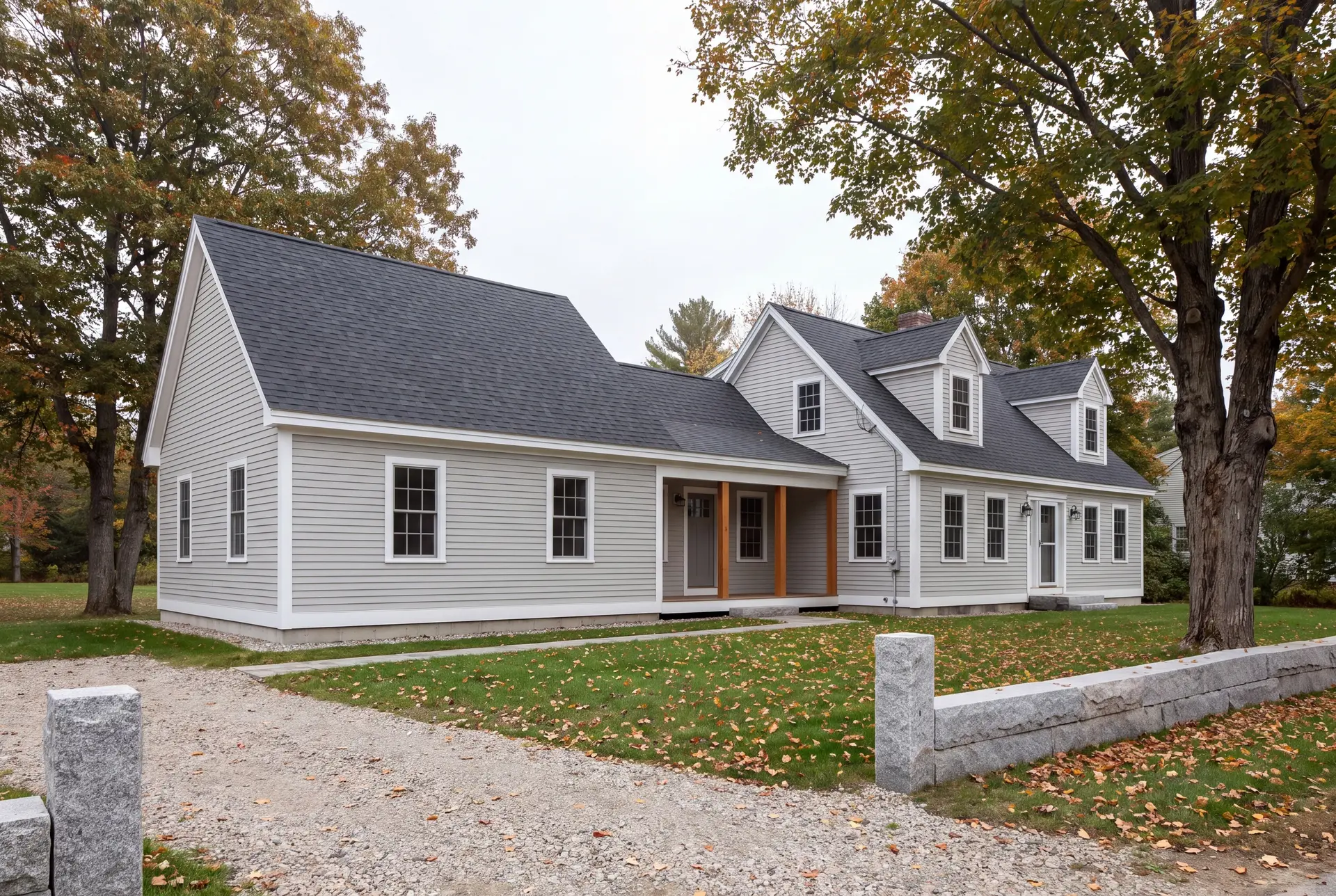 Illustration: An exterior view of a light gray clapboard house with a new single-story addition, featuring a dark gray roof and autumn trees
