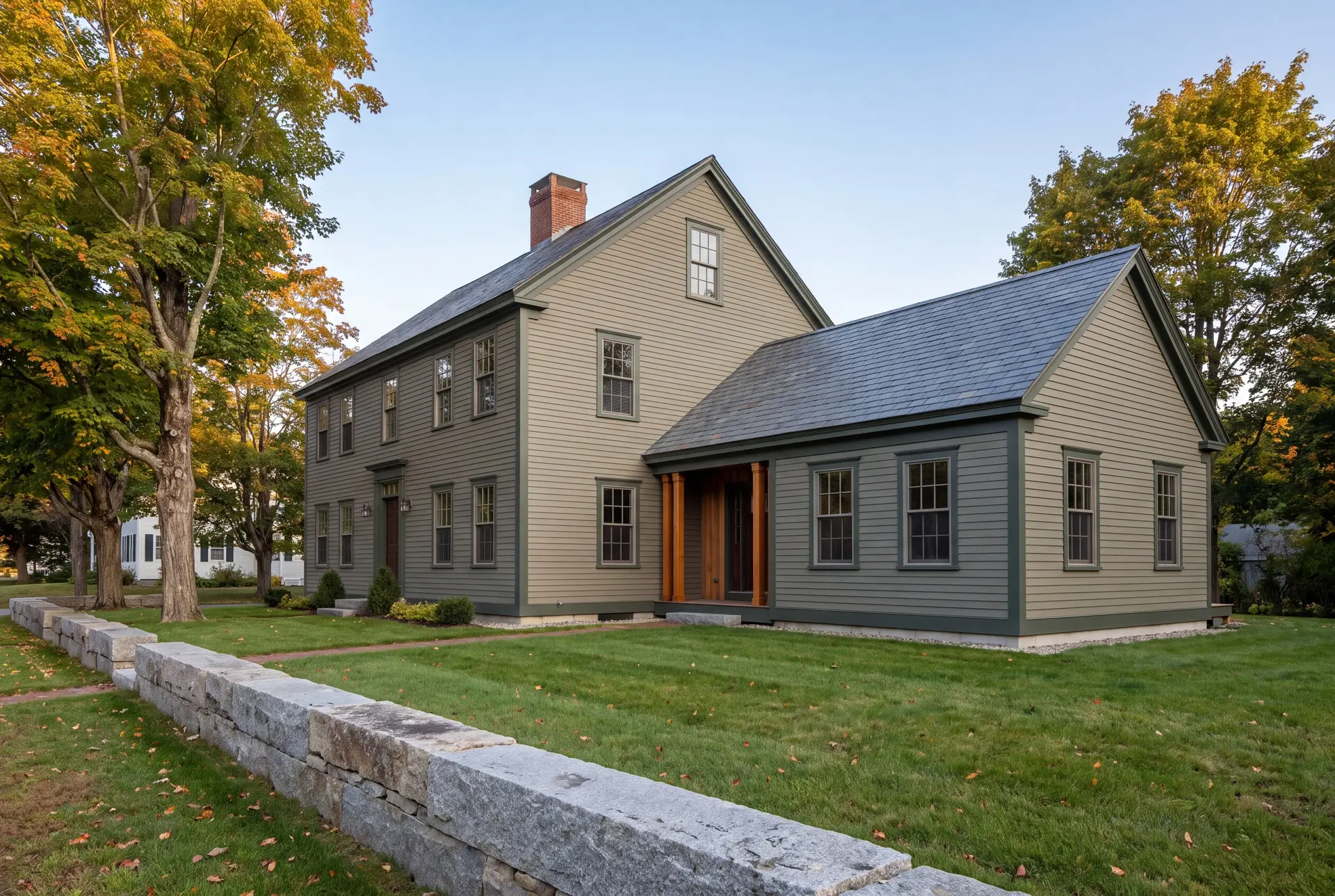 Illustration: An exterior three-quarter view of a two-story Colonial house with a new single-story addition, both in olive clapboard siding, with a green lawn and stone wall in the foreground