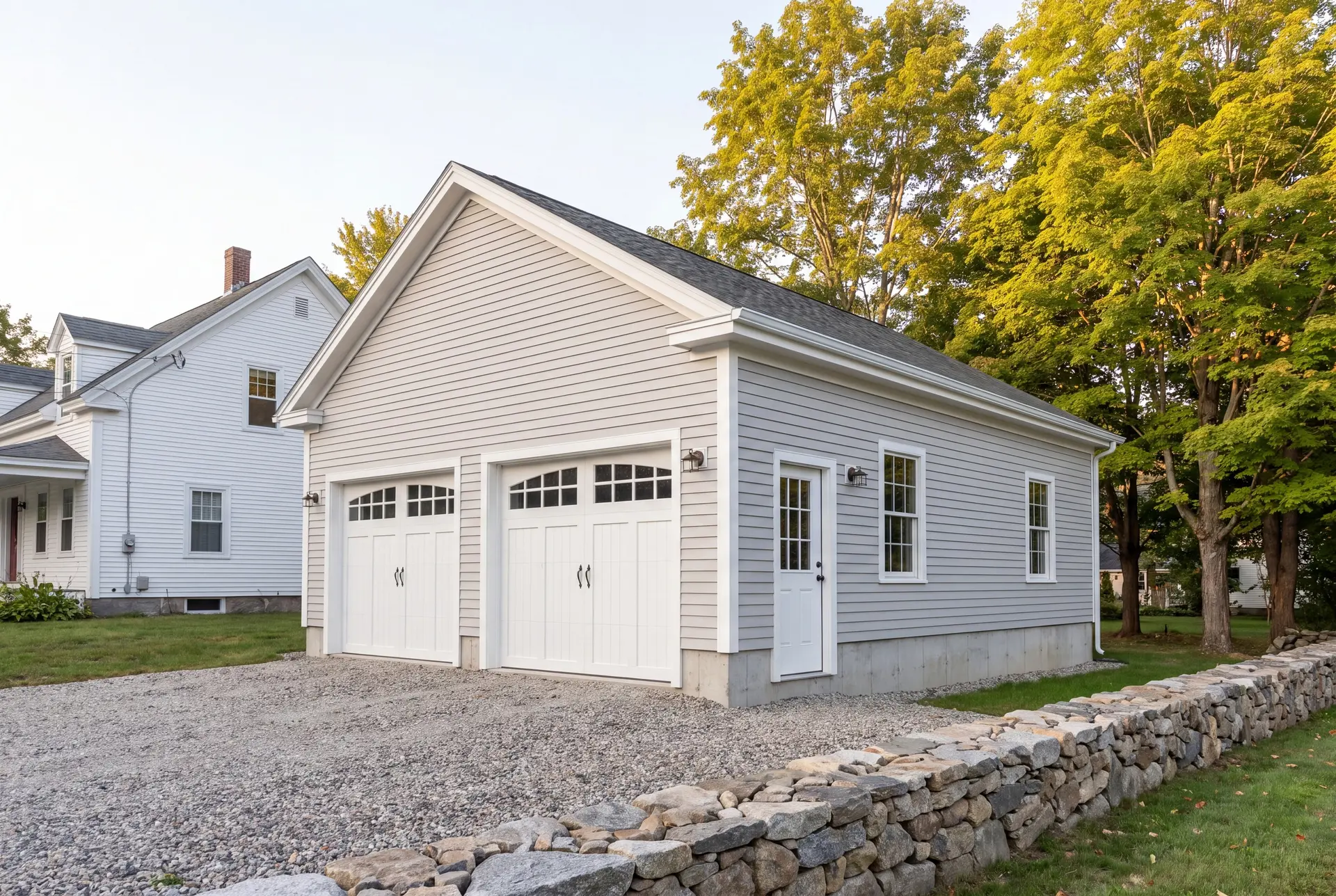 Illustration: A newly built light gray two-car garage with white doors and trim, a gravel driveway, and a stone wall