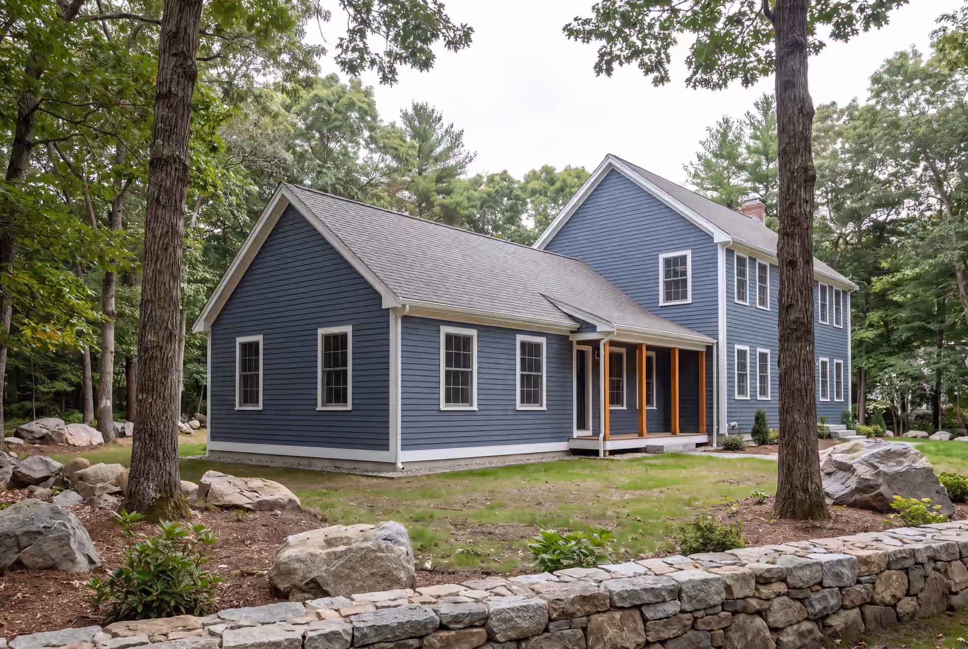 home addition builder in Scarborough, ME: illustrative scene, A blue clapboard house with a new single-story addition and a covered porch, surrounded by trees and rocks