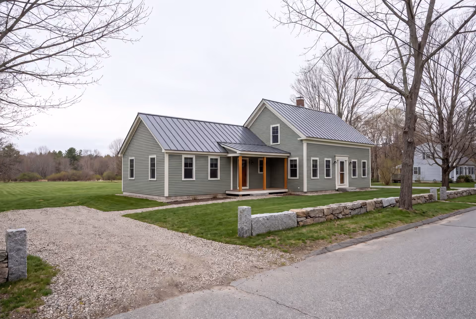 home addition builder in Standish, ME: illustrative scene, An exterior three-quarter view of a sage green farmhouse with a new addition, featuring a dark metal roof and a covered porch with wooden posts