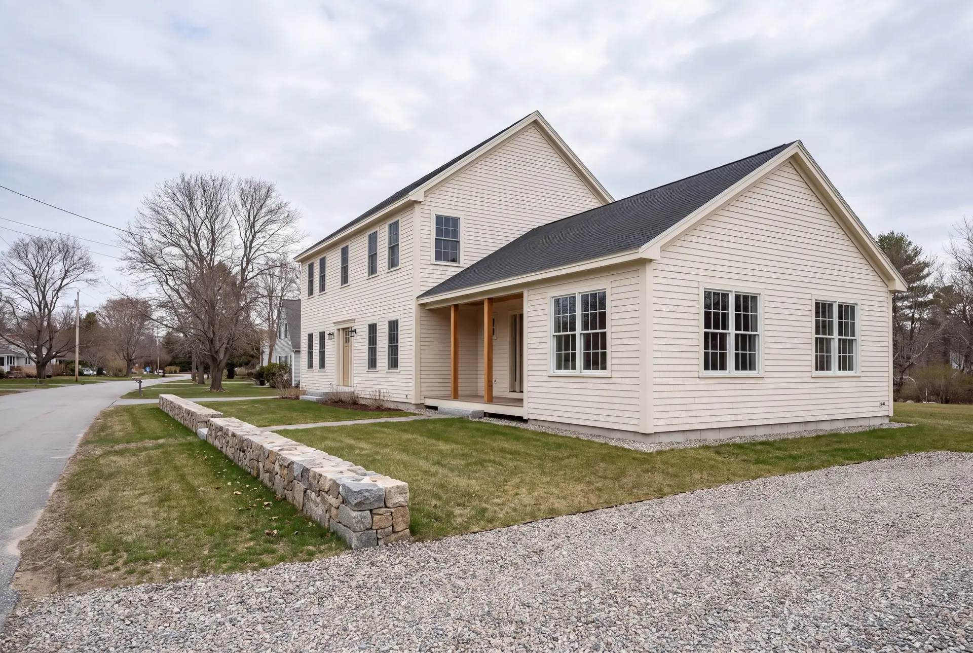 Illustration: A pale cream clapboard house with a new single-story addition, viewed from a three-quarter exterior angle, showing a gravel driveway and a stone wall in the foreground