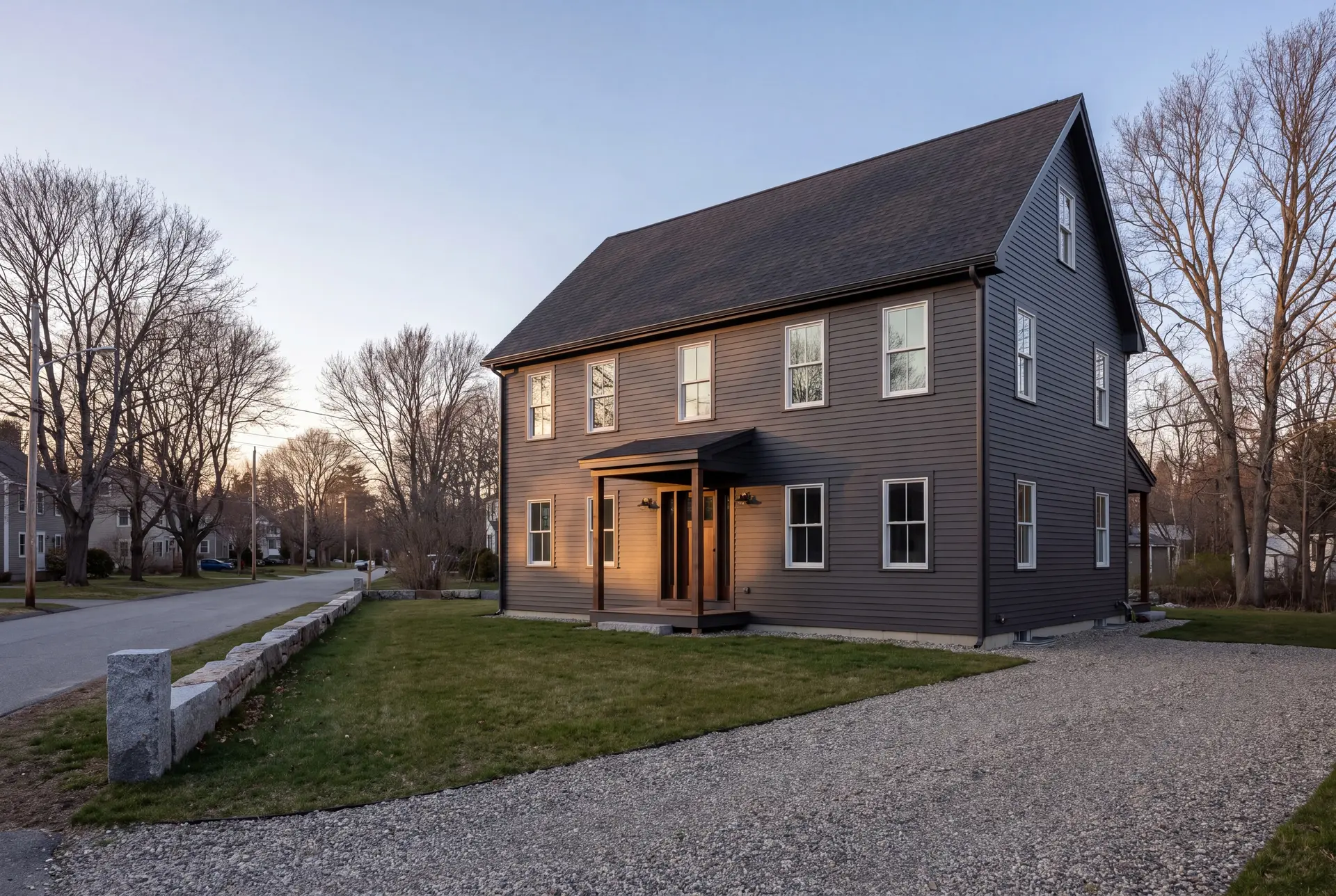 cost to build a house in Portland, Maine: illustrative scene, A newly built dark charcoal farmhouse with white windows and a covered entry, viewed from a three-quarter angle on a sunny day