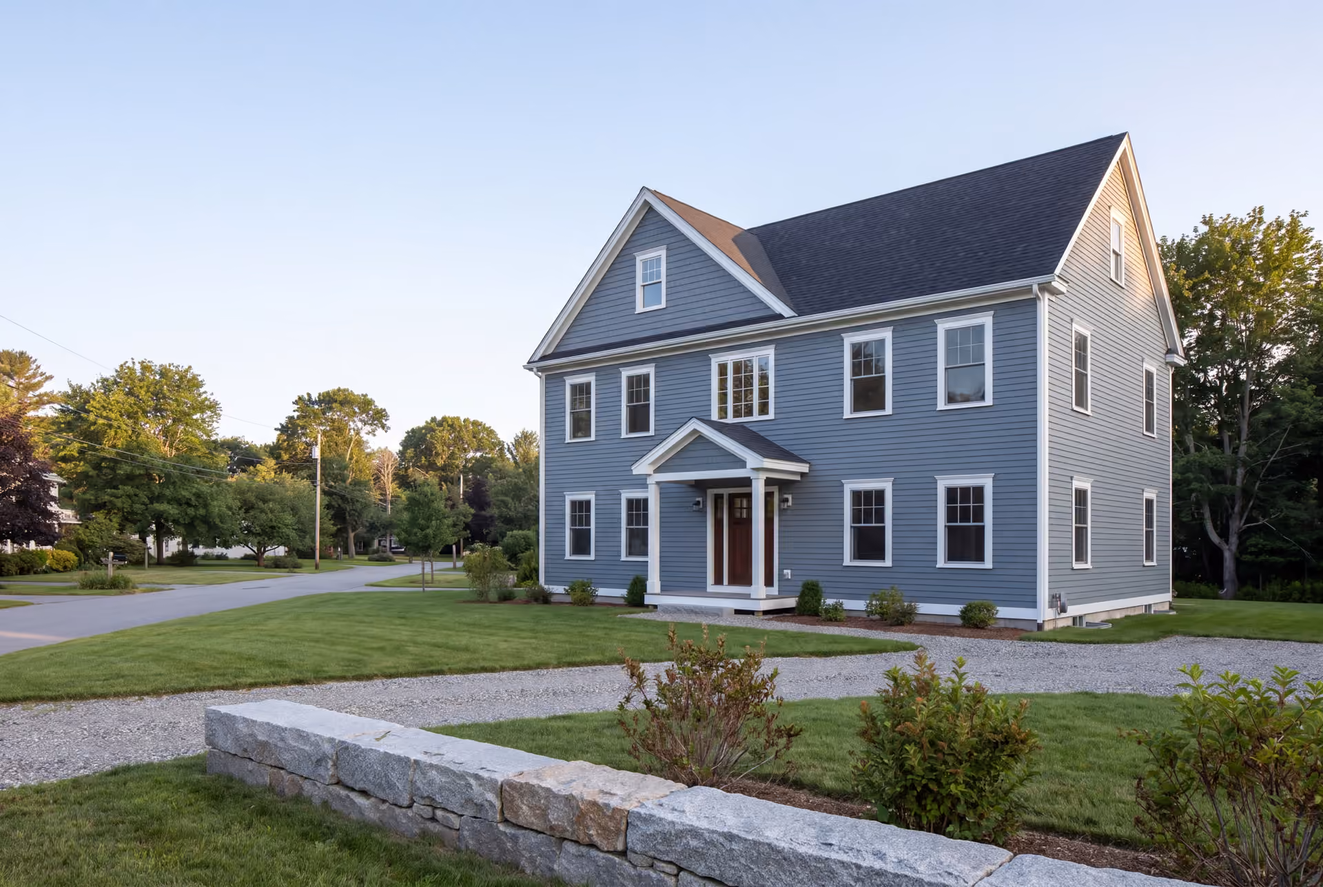 custom home builder in Buxton, ME: illustrative scene, A newly built two-story house with blue-gray siding, a dark shingled roof, and white-trimmed windows, viewed from the front and side
