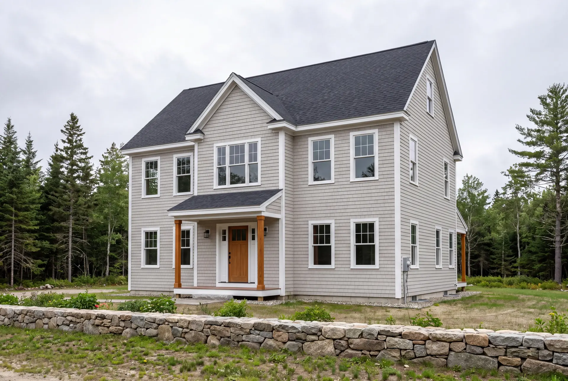 Illustration: A newly built two-story shingle-style house with light gray siding, a dark roof, and a covered front entry, set against a backdrop of trees and a stone wall