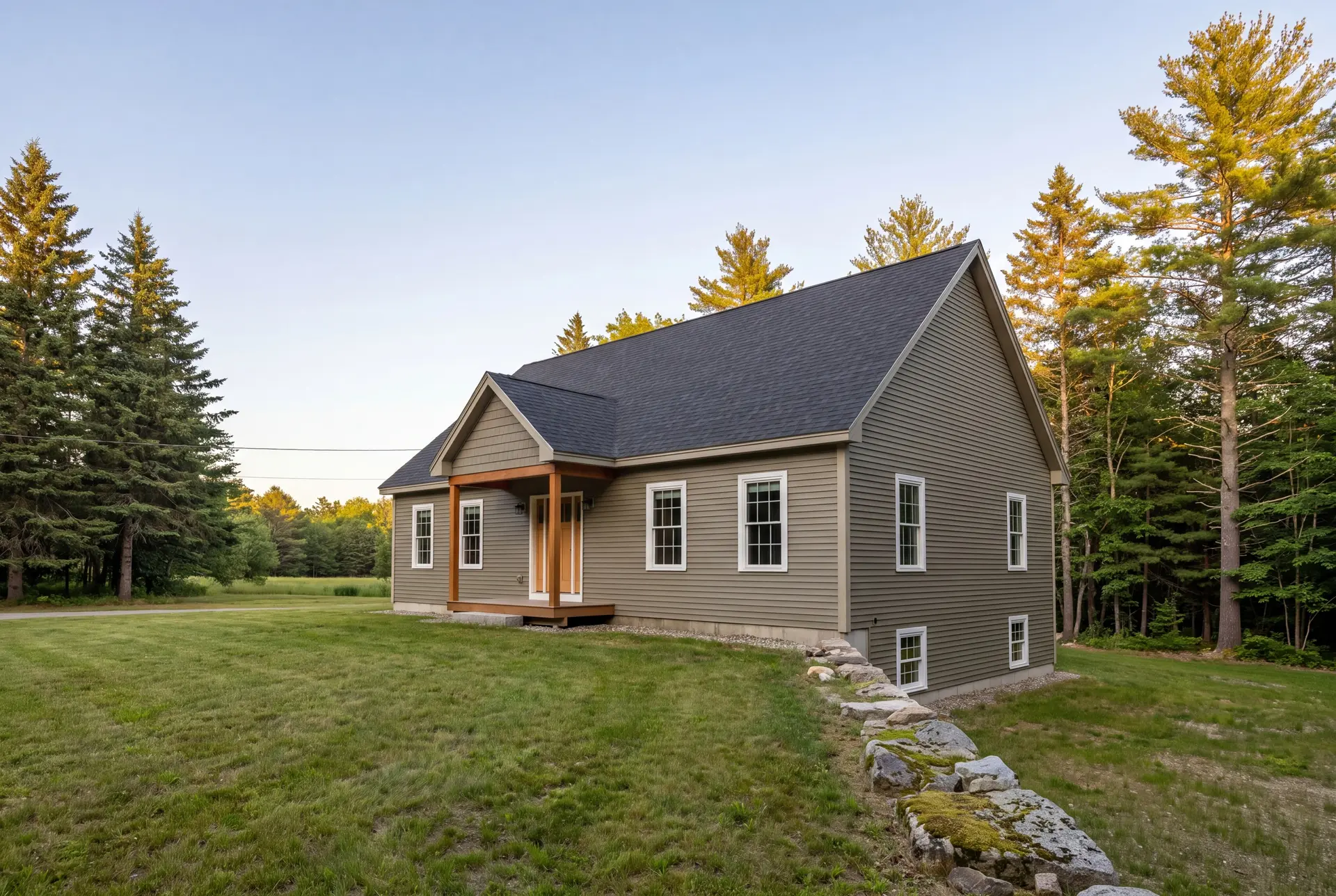 Illustration: A newly built olive green ranch house with a dark gray roof, white windows, and a wooden porch, set in a grassy area with pine trees