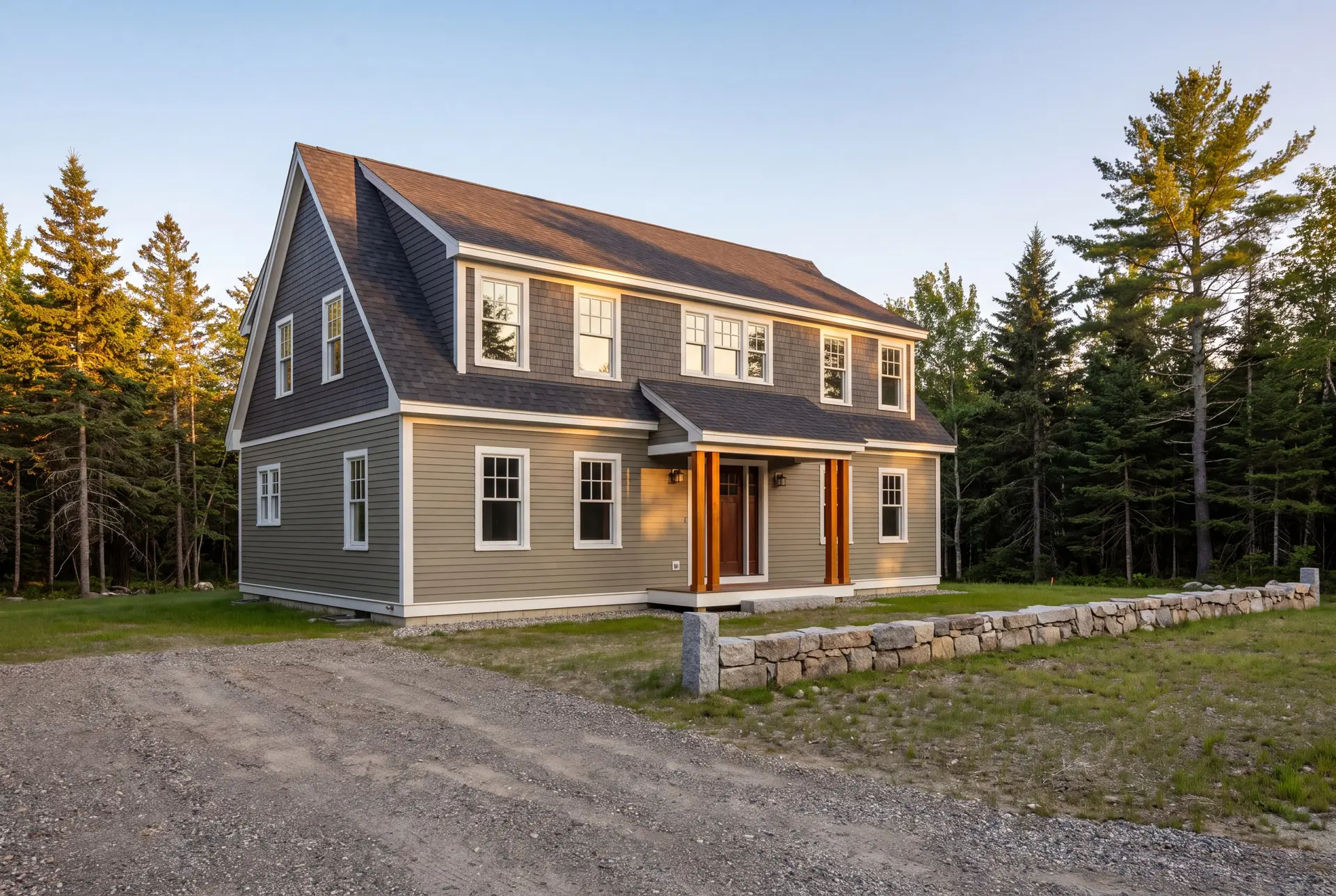 Illustration: A newly built two-story shingle-style house with olive clapboard and gray shingle siding, a dark shingled roof, and white-trimmed windows, set against a backdrop of evergreen trees