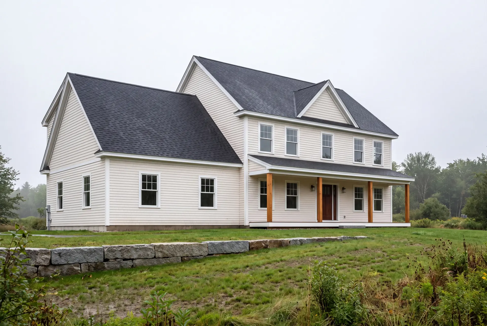 Illustration: A newly built two-story shingle-style house with light siding, a dark roof, and a covered porch with wooden posts, set in a grassy field