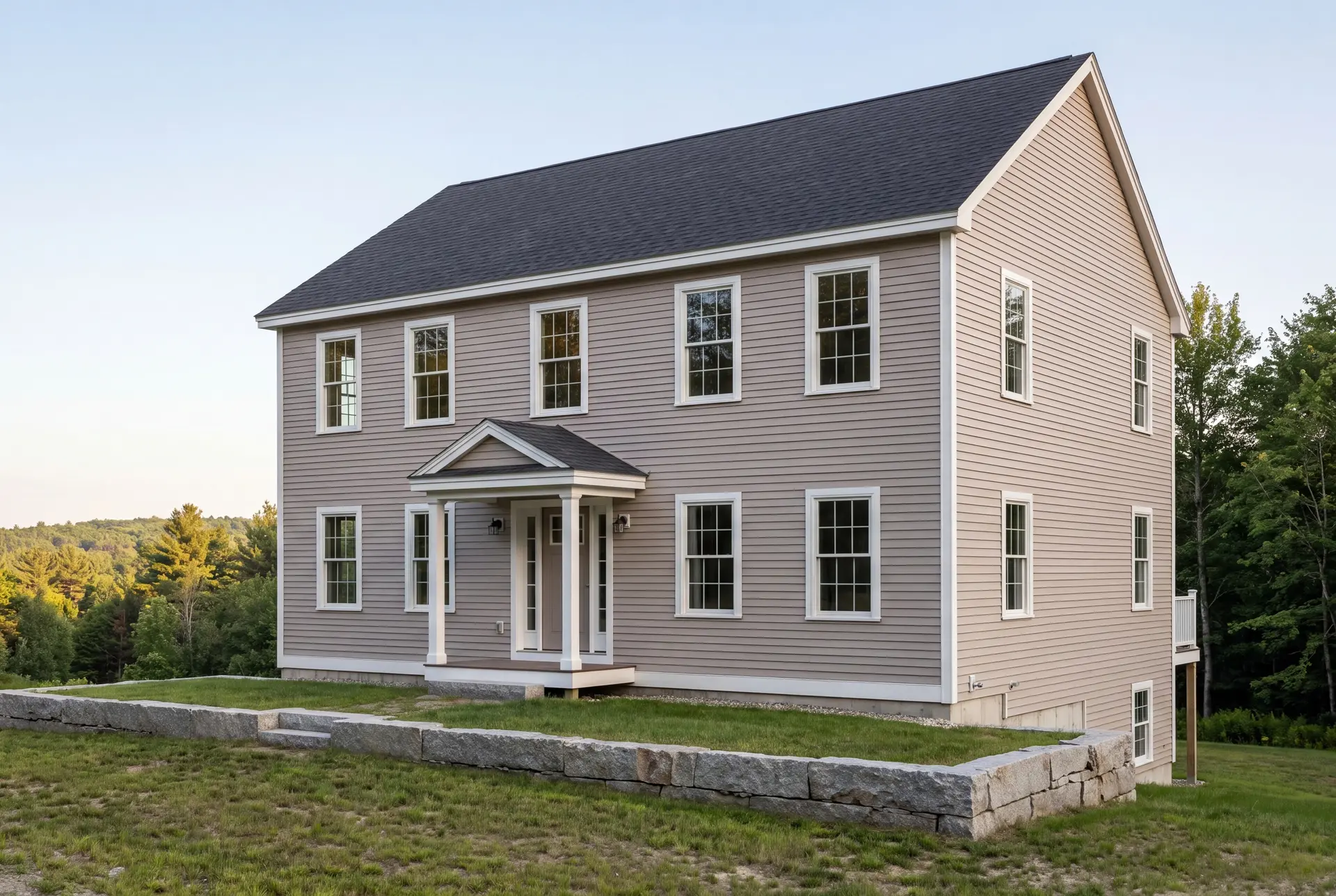 Illustration: A newly built two-story Colonial house with light brown siding and a dark gray roof, viewed from the front and side, with a stone wall in the foreground and trees in the background