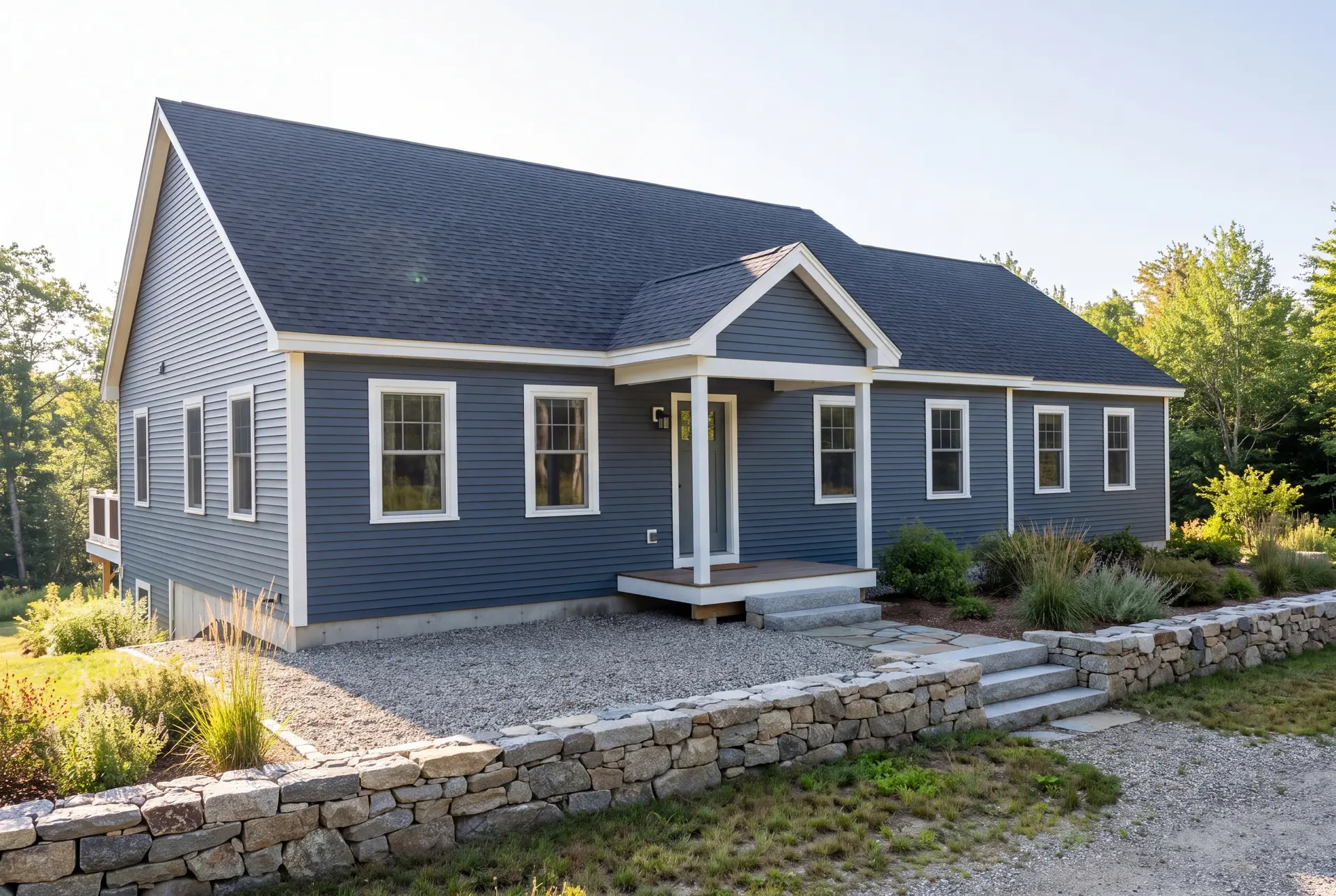 Illustration: A newly built one-story ranch house with blue siding, a dark roof, and white trim, seen from a three-quarter angle with a stone wall and landscaping in the foreground