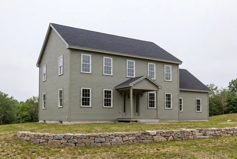 Illustration: A newly built two-story Colonial house with sage green siding and a dark gray roof, viewed from a three-quarter angle