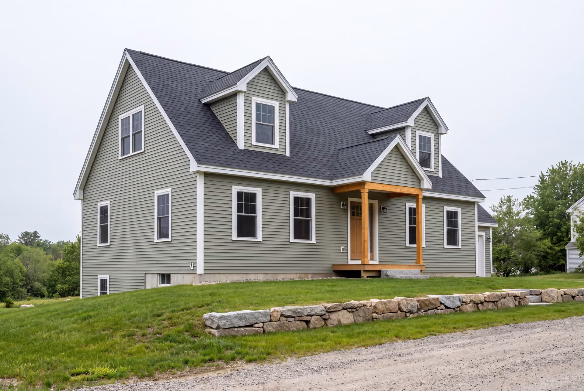 custom home builder in Old Orchard Beach, ME: illustrative scene, A newly built Cape house with sage green siding and a dark roof, seen from a three-quarter view on a grassy hill