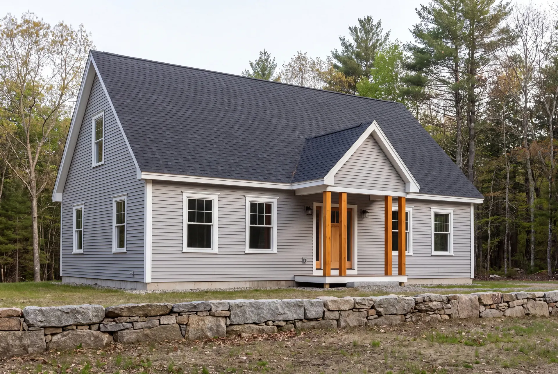 Illustration: A newly built gray house with a dark roof and a wooden front porch, surrounded by a stone wall and trees