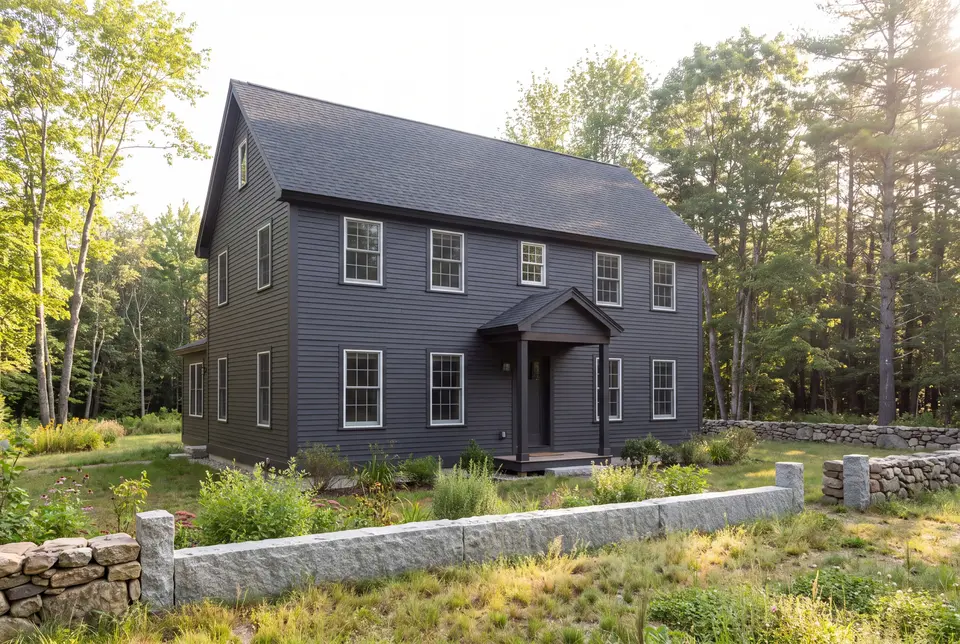 Illustration: A dark charcoal farmhouse with white-trimmed windows and a covered entry, surrounded by trees and a stone wall