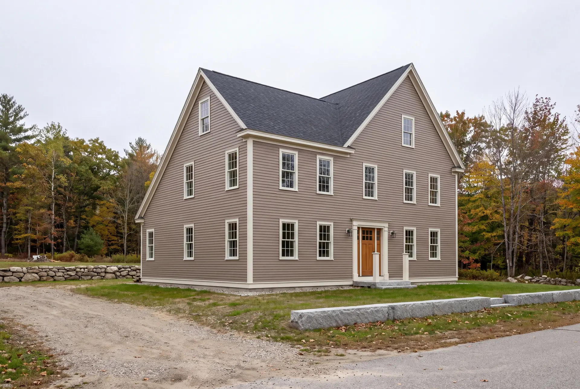 Illustration: A newly built two-story New England saltbox house with taupe siding and a dark roof, surrounded by autumn trees and a gravel driveway