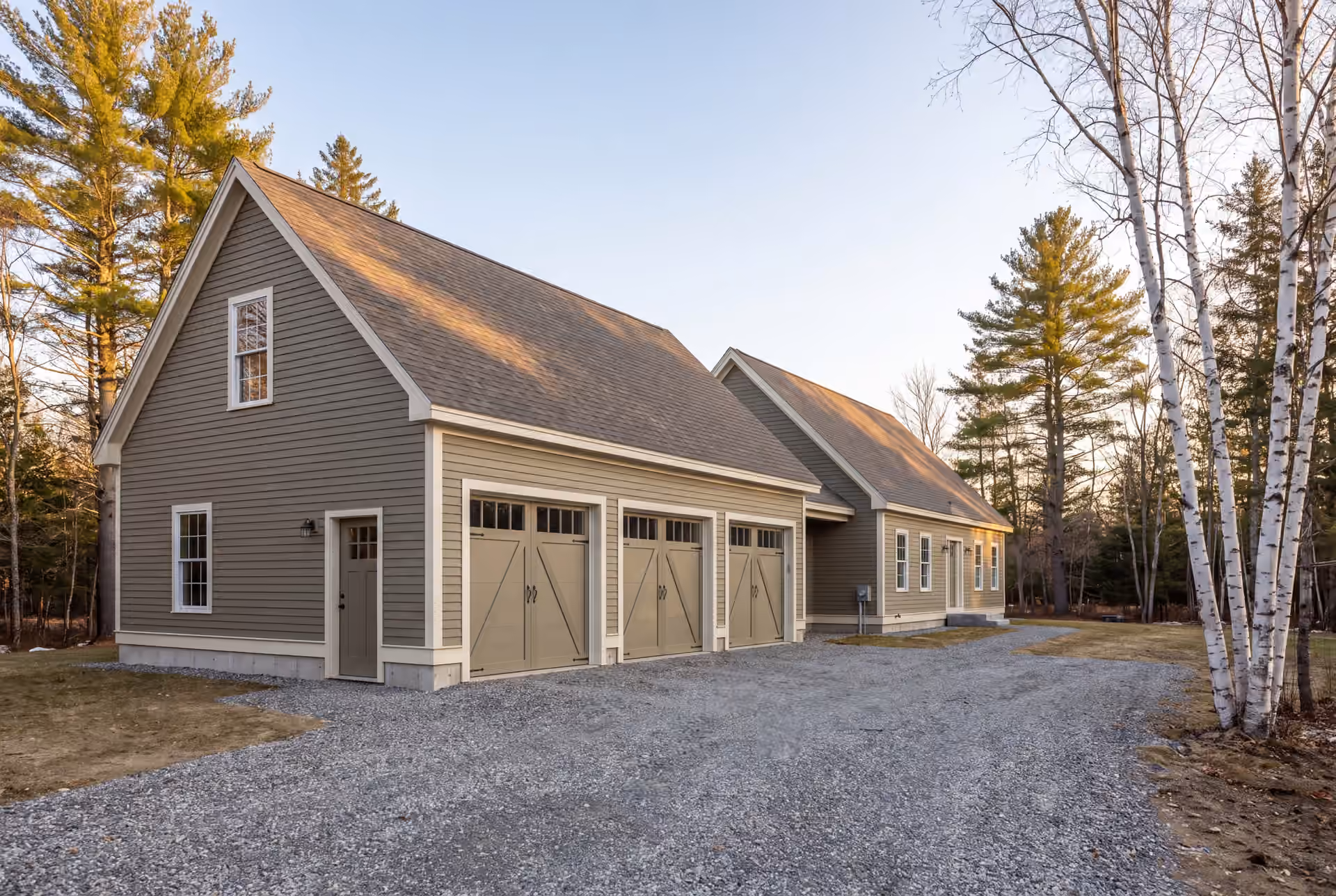 garage builder: illustrative scene, A newly built three-bay garage and attached house with dusty olive siding and a gravel driveway, surrounded by trees