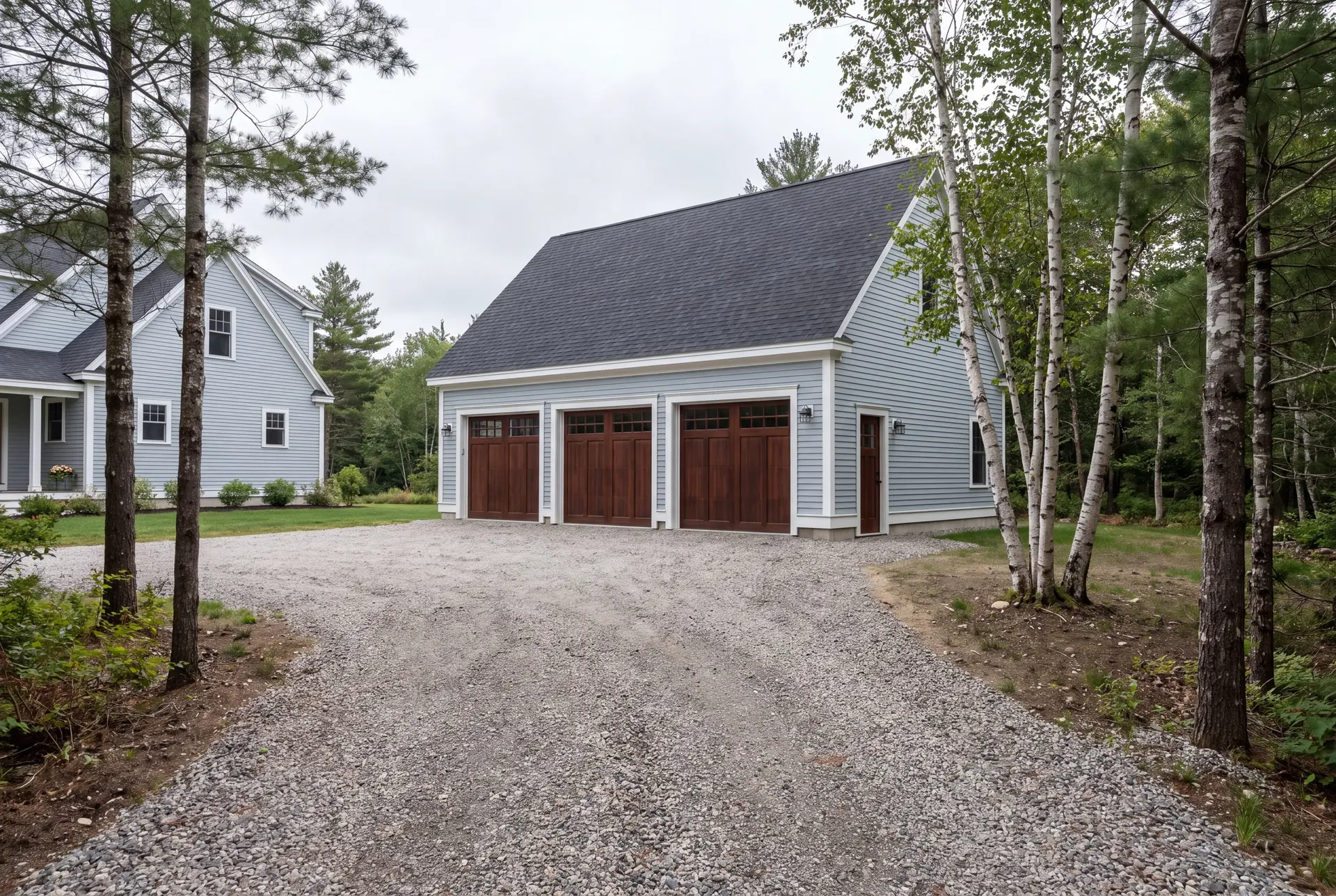 Illustration: A newly built light blue garage with three brown garage doors and a gravel driveway, next to a house and surrounded by trees