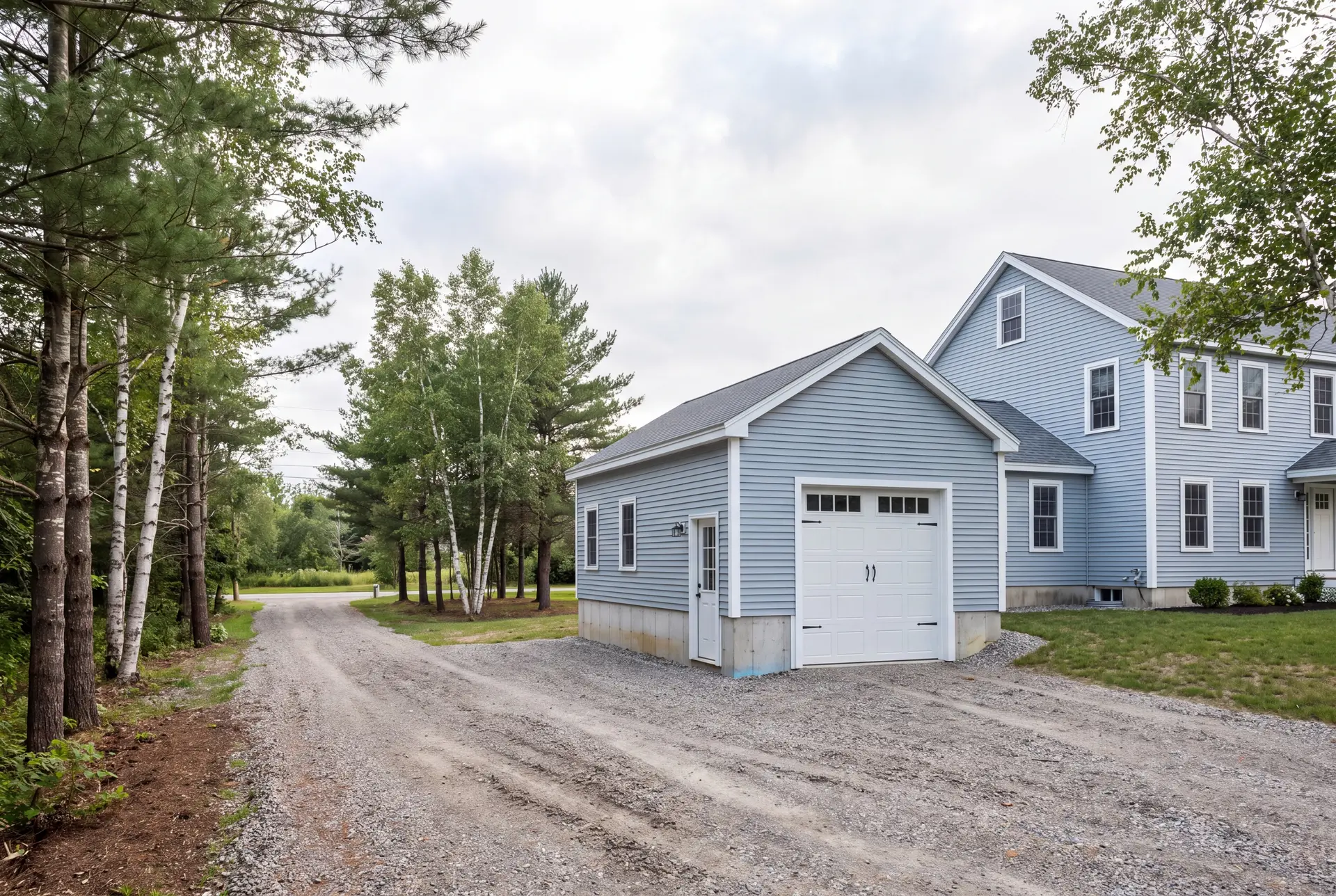 Illustration: A newly built light blue garage with a white door and gravel driveway next to a matching house