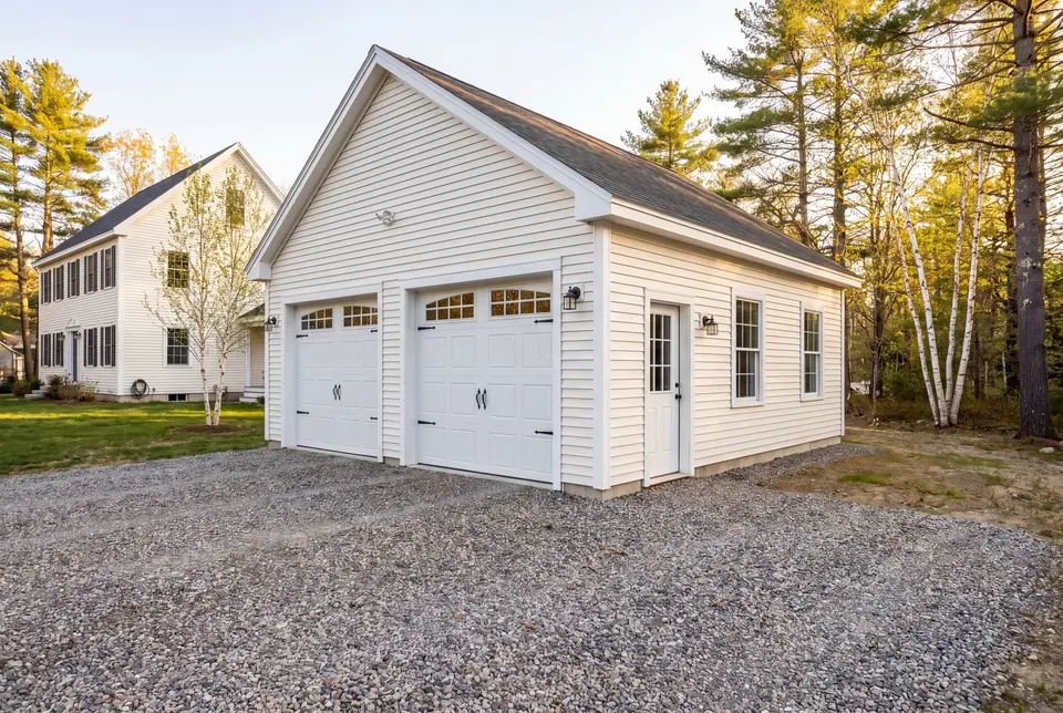 Illustration: A newly built white two-car garage with a gravel driveway next to a house and trees