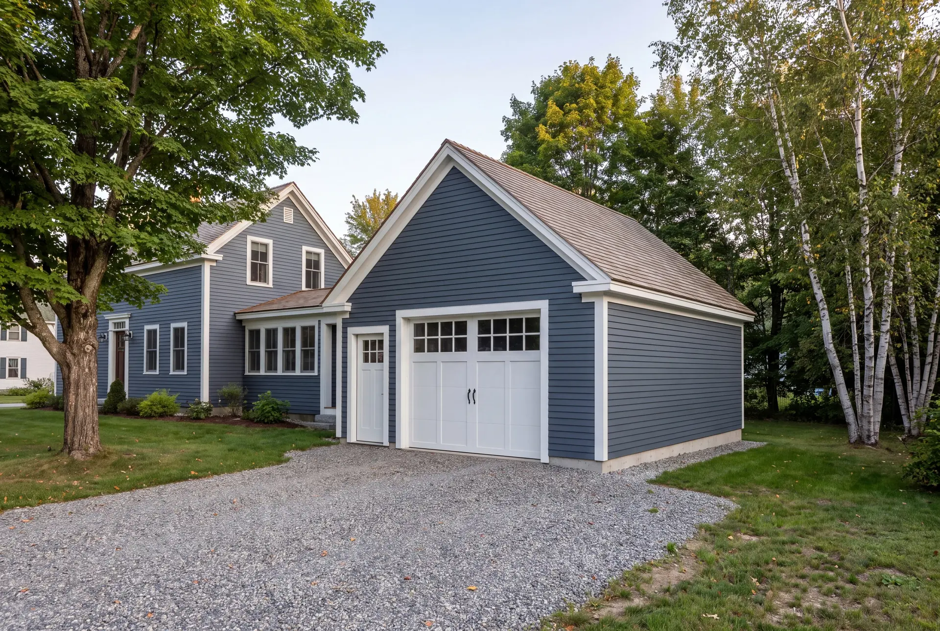 Illustration: A newly built, detached single-bay garage with blue siding and a white carriage-style door, next to a matching house, with a gravel driveway