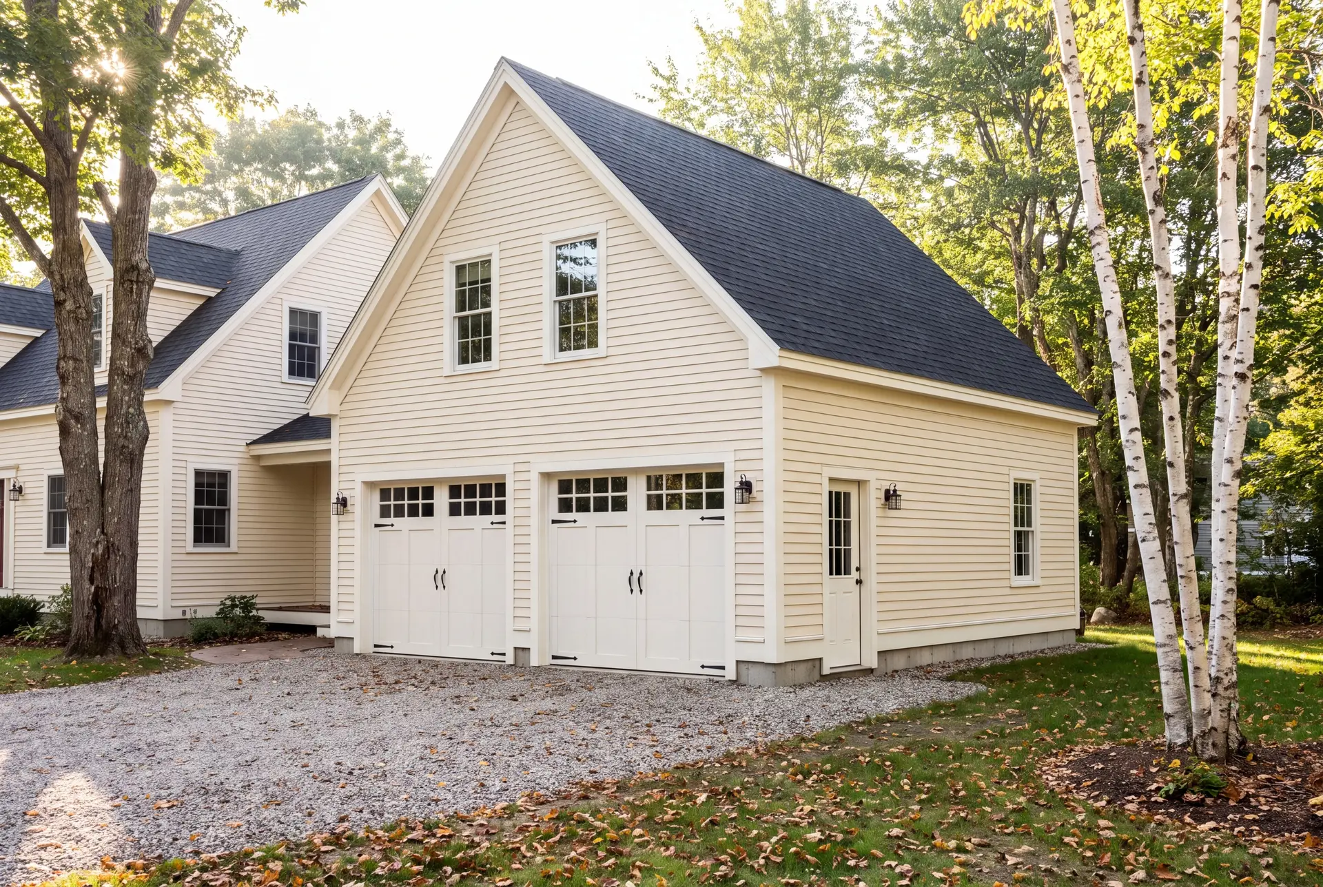 Illustration: A newly built two-bay garage with ivory siding and a dark roof, attached to a house, with a gravel driveway and surrounding trees