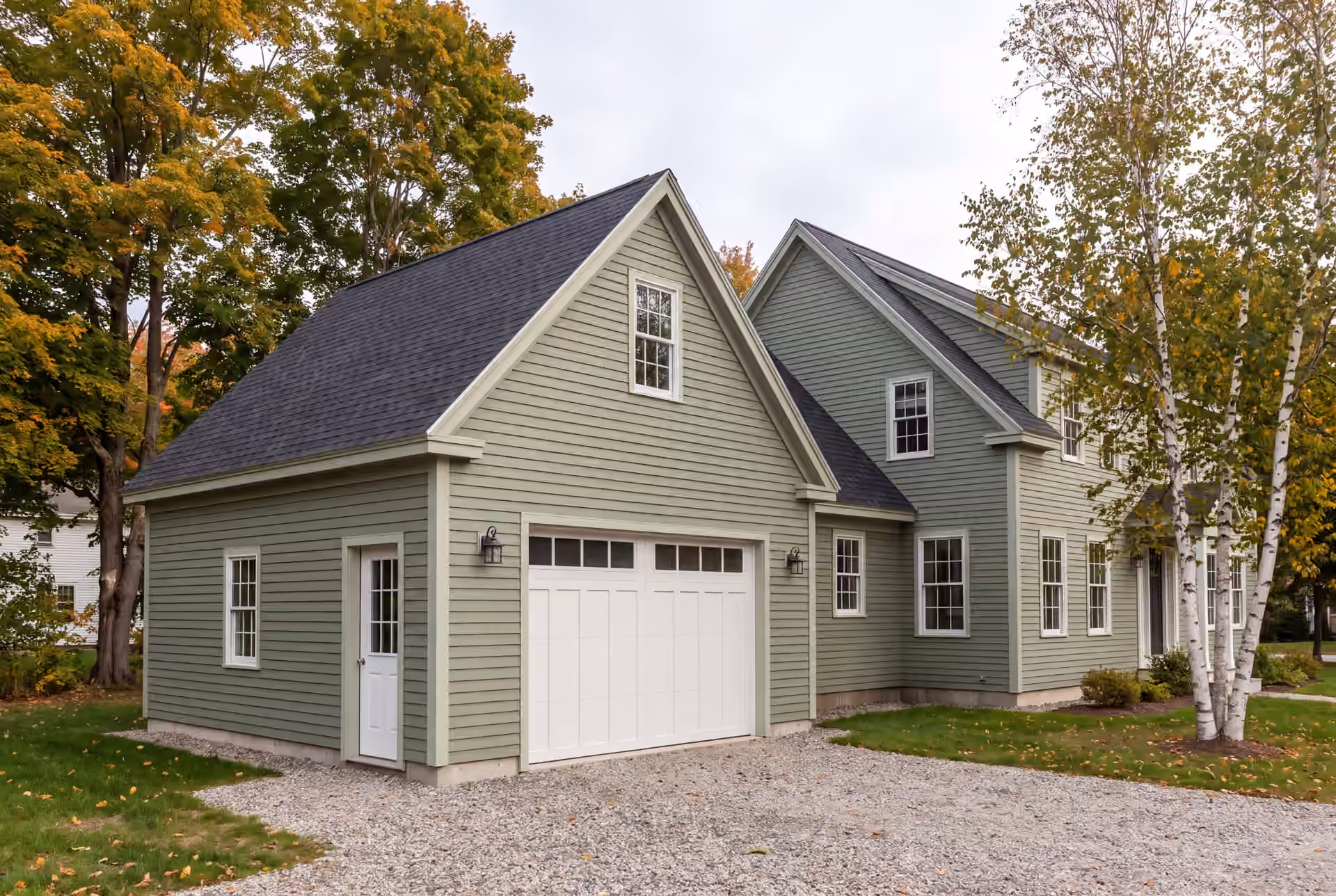garage builder in Freeport, ME: illustrative scene, A newly built sage green garage attached to a house, with a gravel driveway and autumn trees