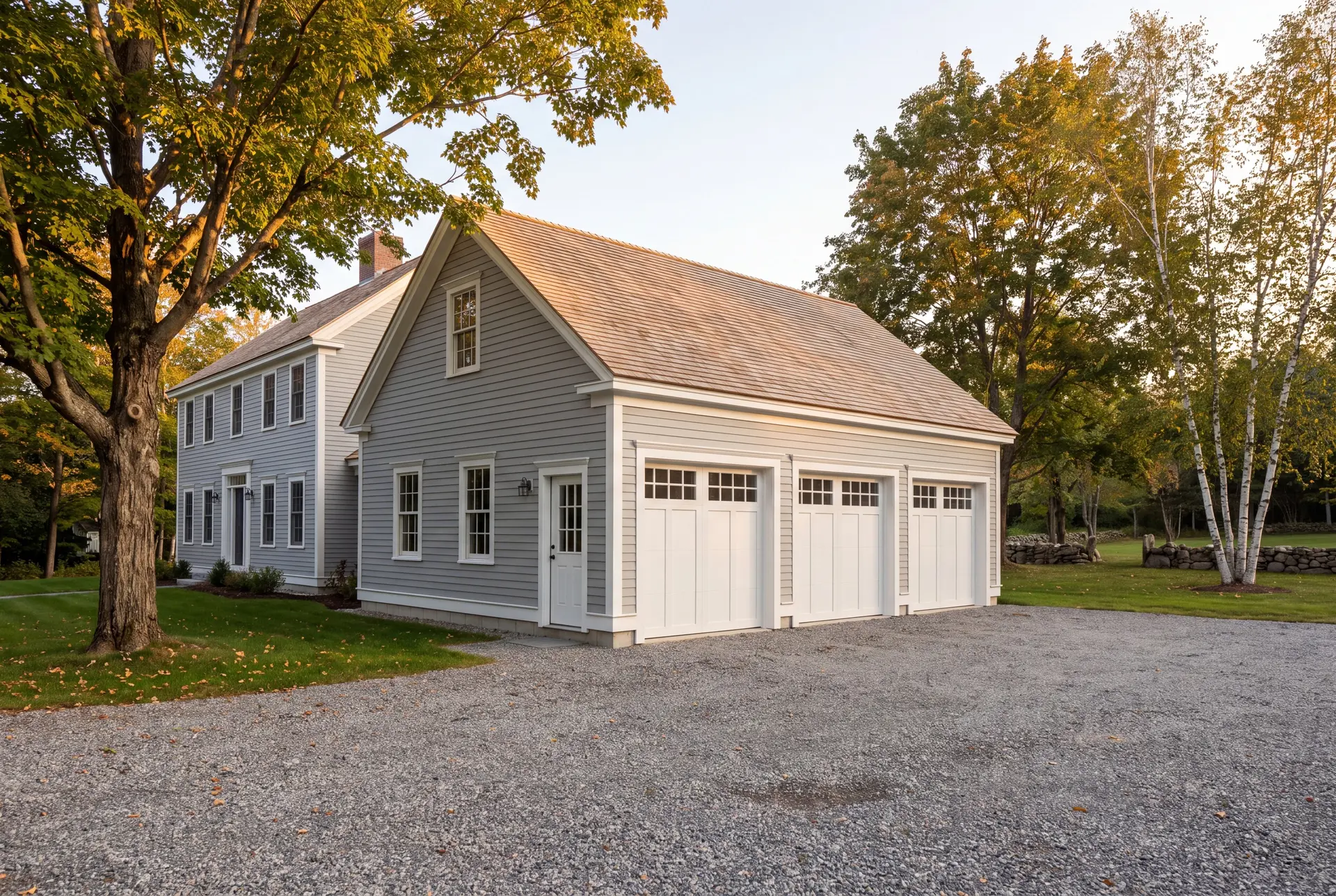 Illustration: A newly built three-bay garage with light gray siding and a shingle roof, attached to a matching house, with a gravel driveway and surrounding trees