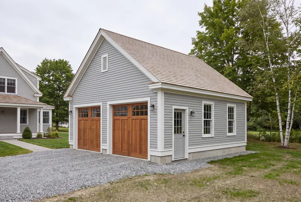 Illustration: A newly built two-bay garage with gray siding and wooden doors, next to a house