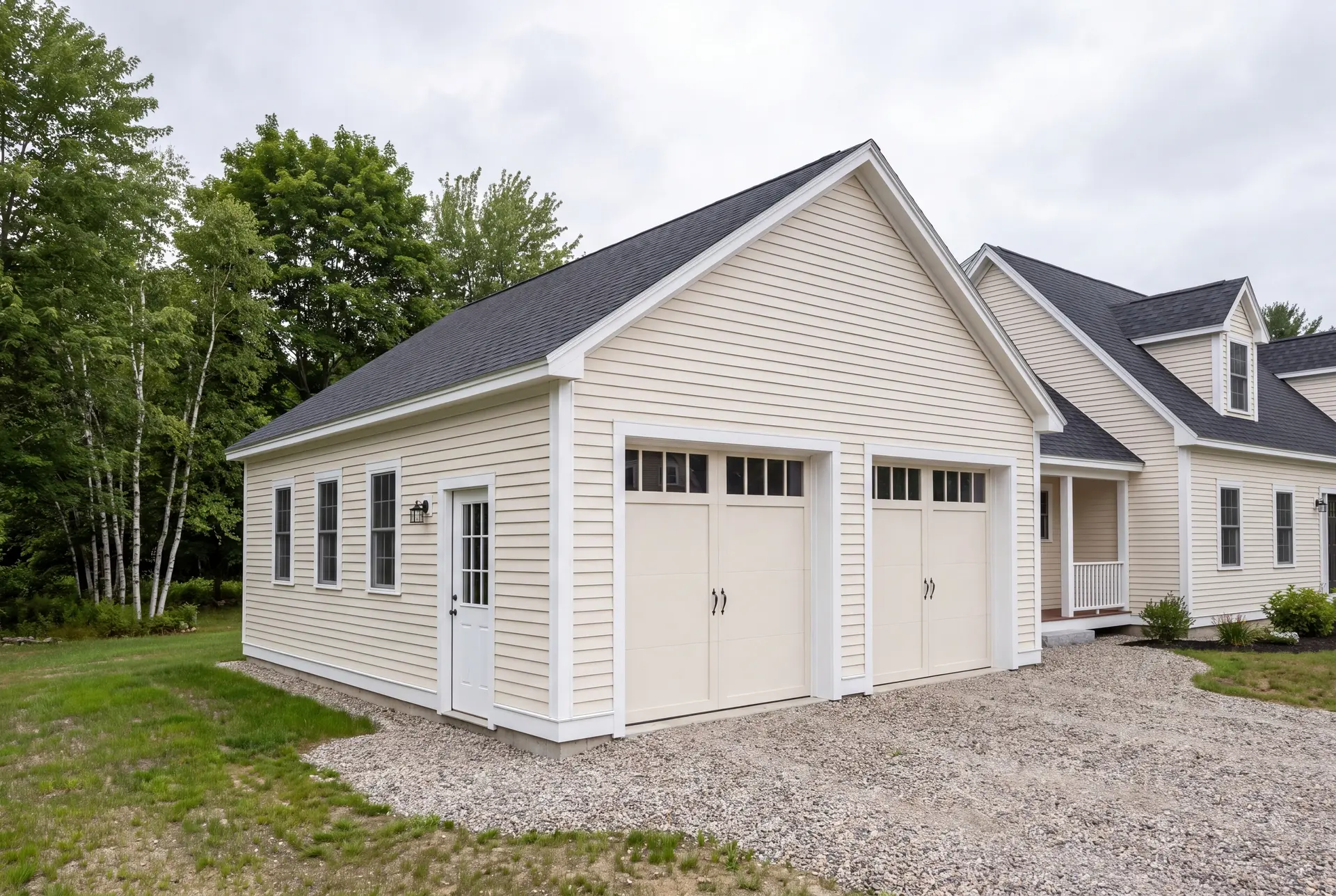 Illustration: A newly built, detached two-bay garage with pale cream siding and a dark roof, next to a matching house, with a gravel driveway
