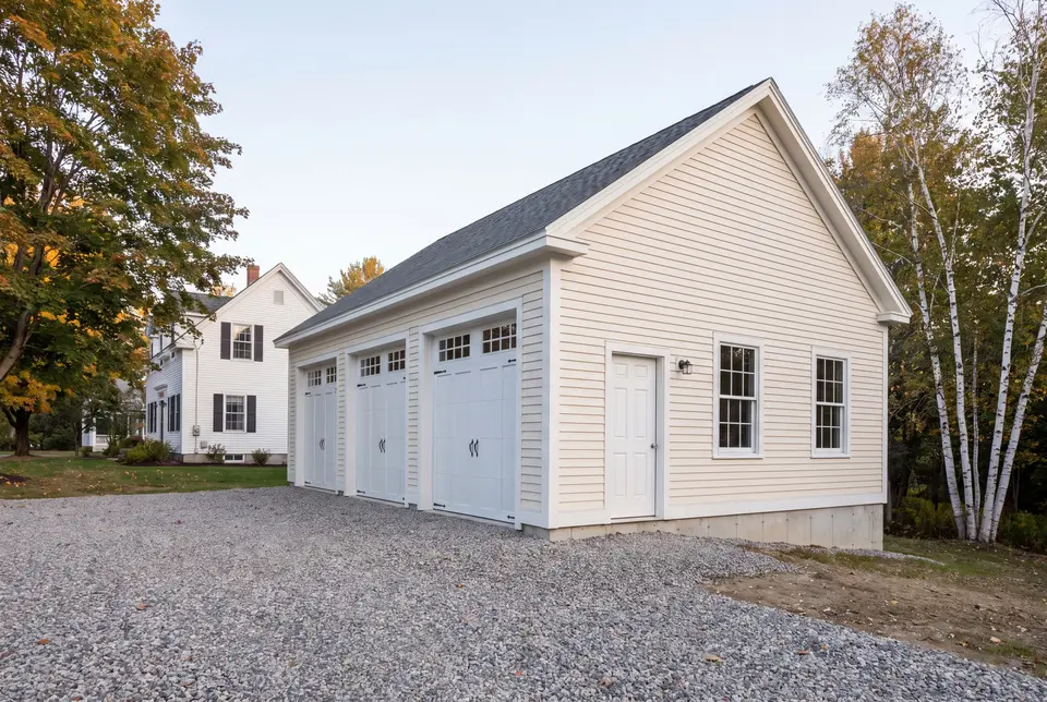 Illustration: A newly built, detached three-car garage with cream siding and a gravel driveway, next to a house and trees
