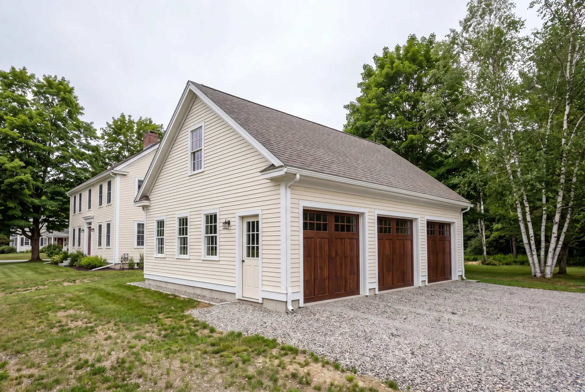 Illustration: A newly built, cream-colored three-car garage with dark wood doors and a gravel driveway, next to a traditional house