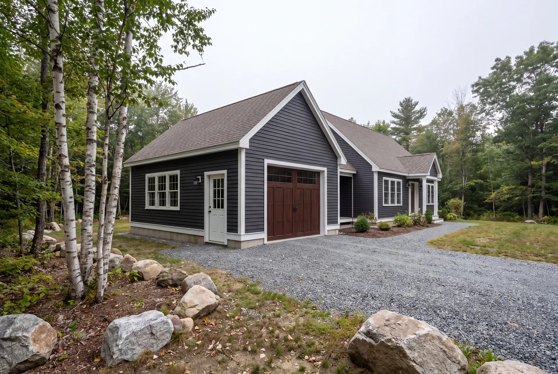Illustration: A newly built dark gray garage with a brown garage door and white trim, next to a matching house, with a gravel driveway and trees