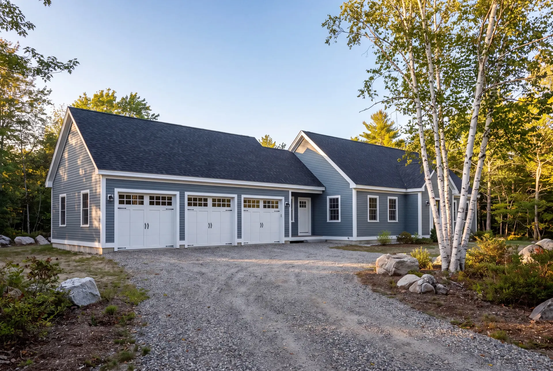 Illustration: A newly built blue-gray house with an attached three-car garage and a gravel driveway, surrounded by trees and rocks under a clear sky