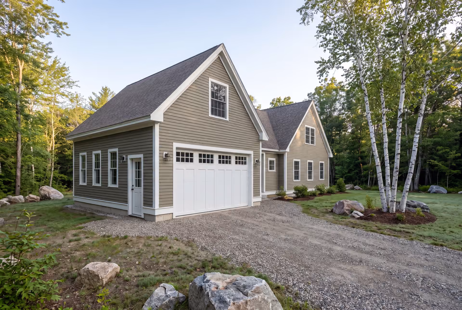 garage builder in Scarborough, ME: illustrative scene, A newly built dusty olive garage and house with a gravel driveway and surrounding trees