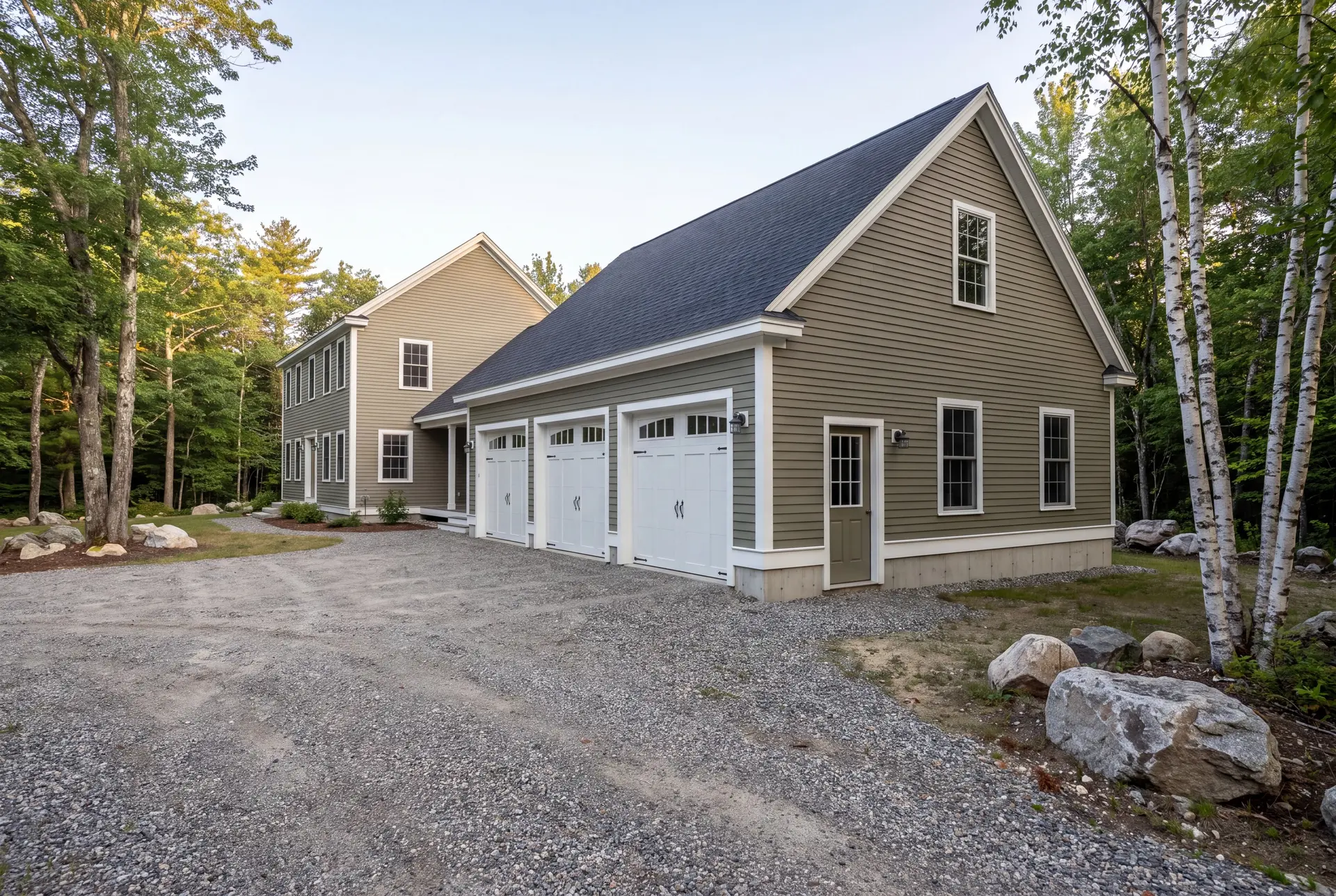 Illustration: A newly built, detached three-bay garage with olive siding and white doors, next to a house, with a gravel driveway and trees