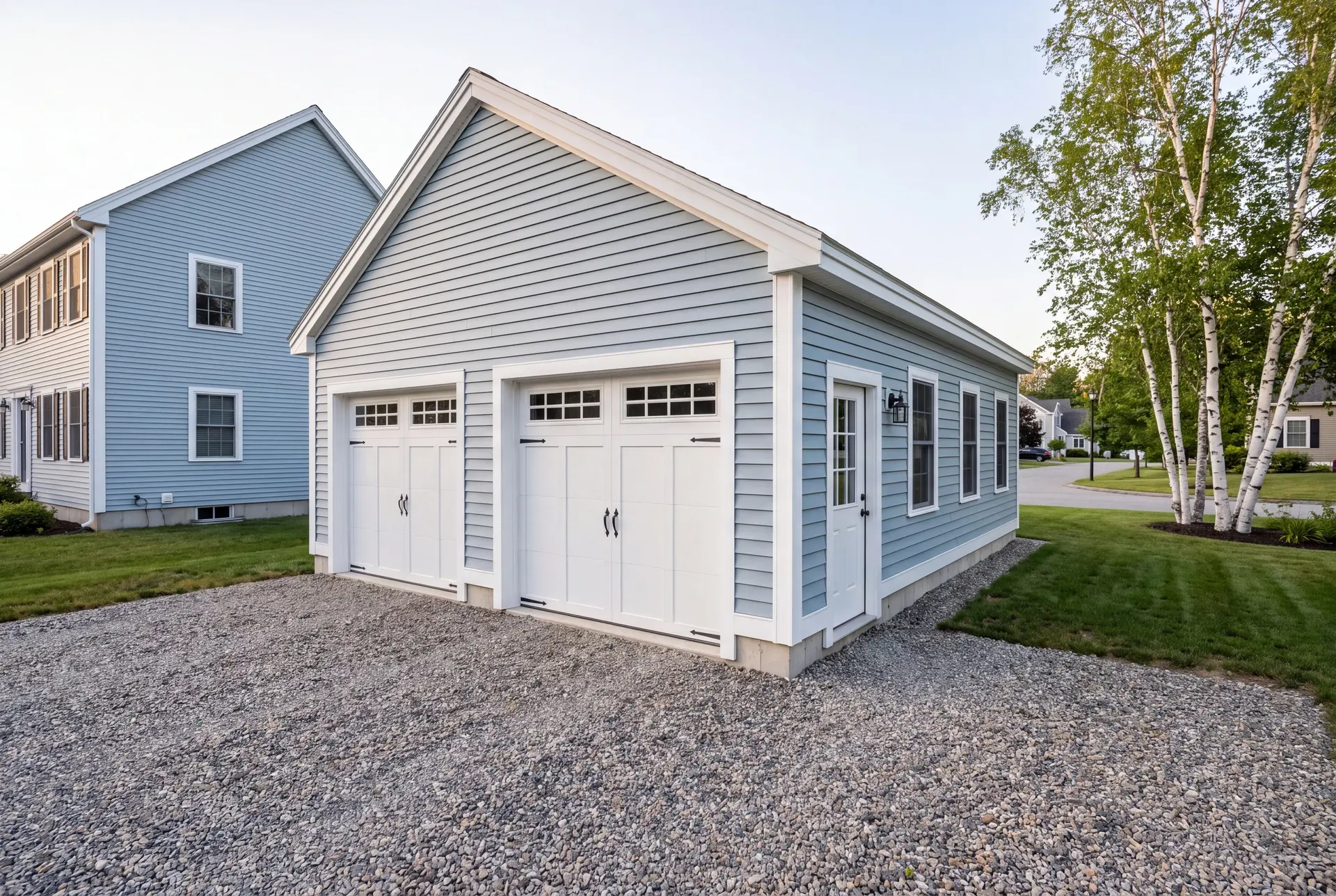 Illustration: A newly built light blue two-car garage with white trim and a gravel driveway, situated next to a matching house