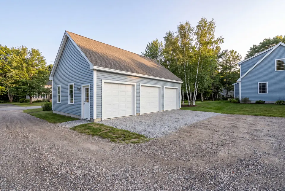 garage builder in Standish, ME: illustrative scene, A newly built light blue garage with three white garage doors and a gravel driveway, next to a matching house