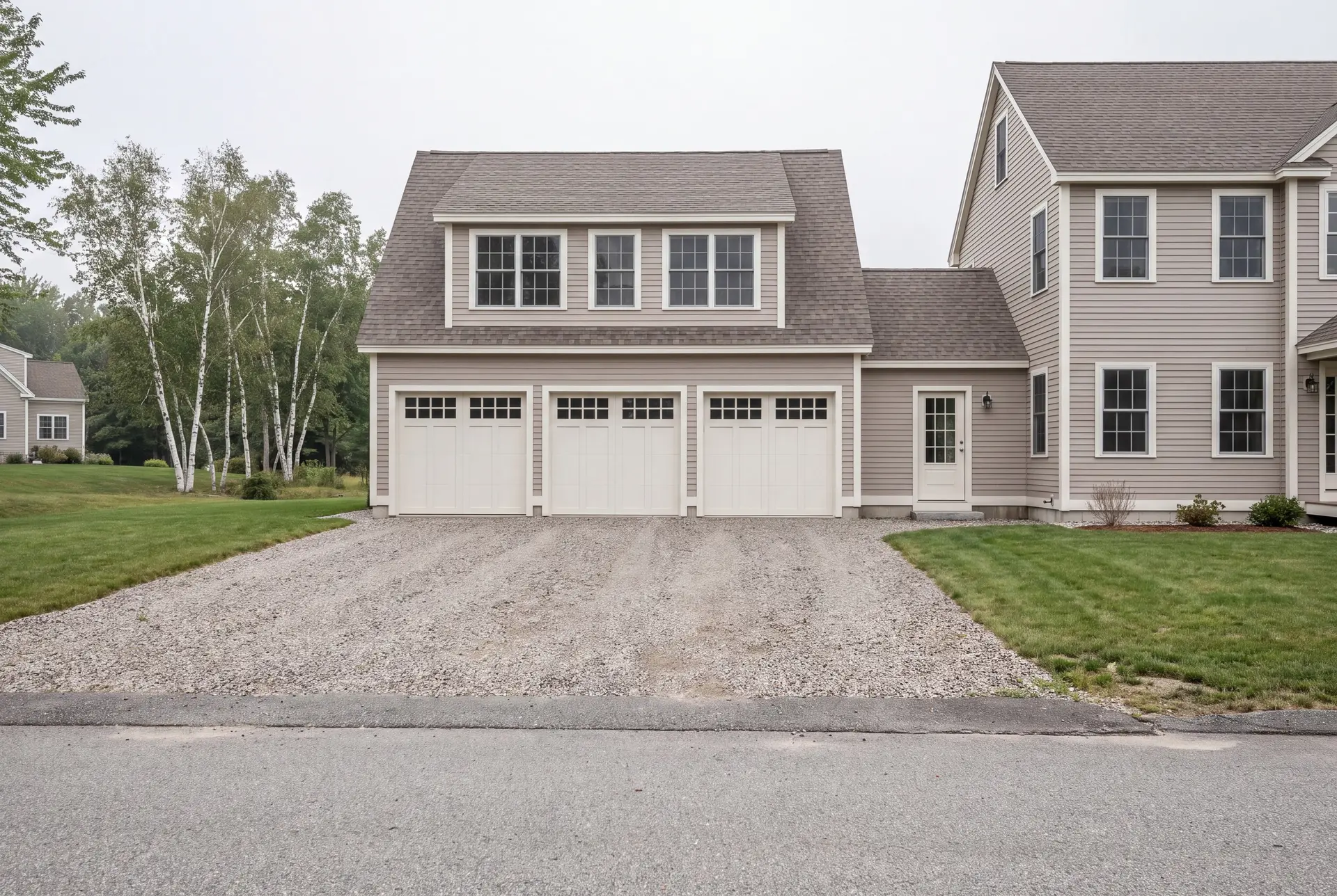 Illustration: A newly built three-bay garage with light mushroom-colored siding and a gray roof, attached to a matching house, with a gravel driveway and green lawns