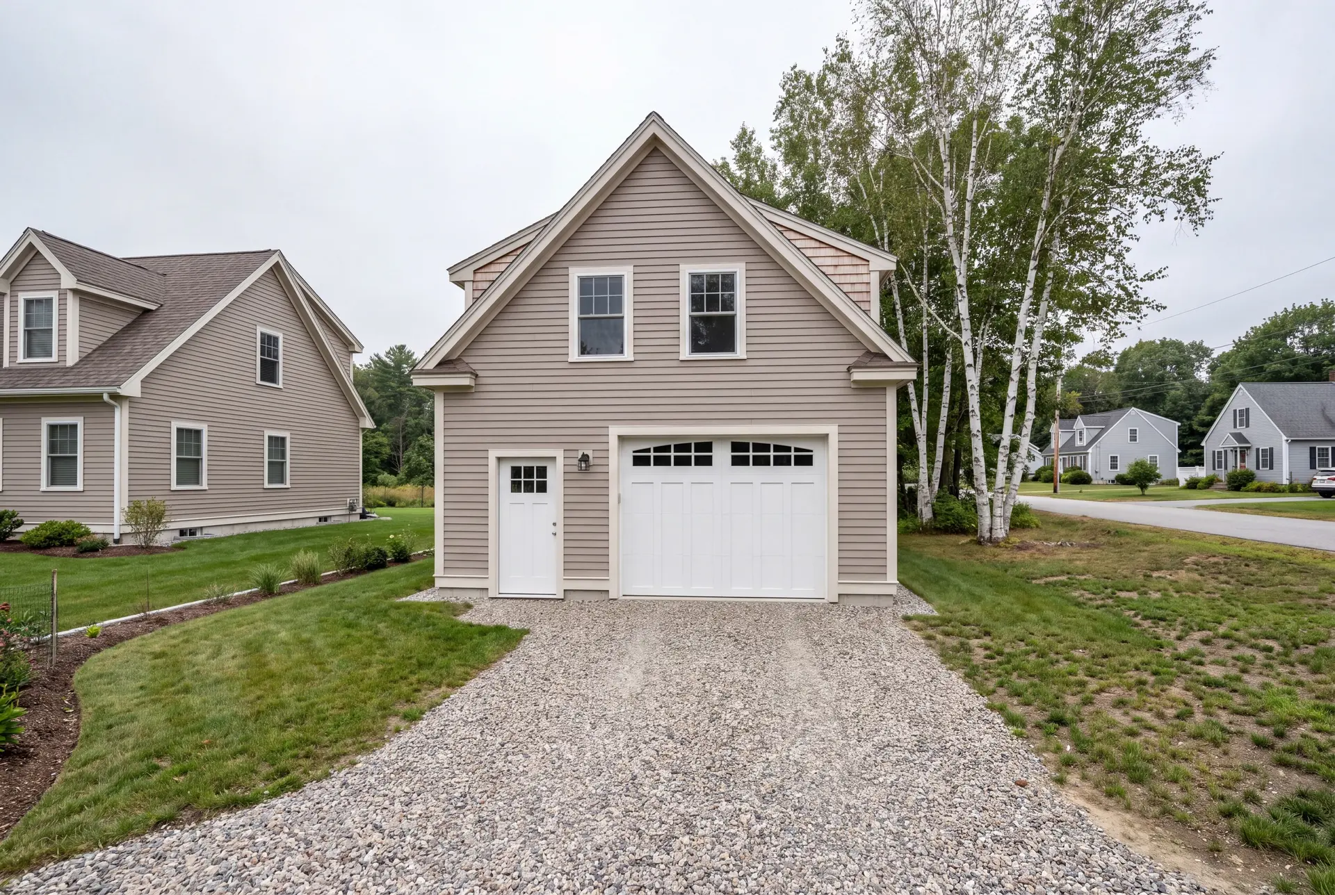 Illustration: A newly built, detached 1-bay garage with mushroom-colored clapboard siding and a gravel driveway