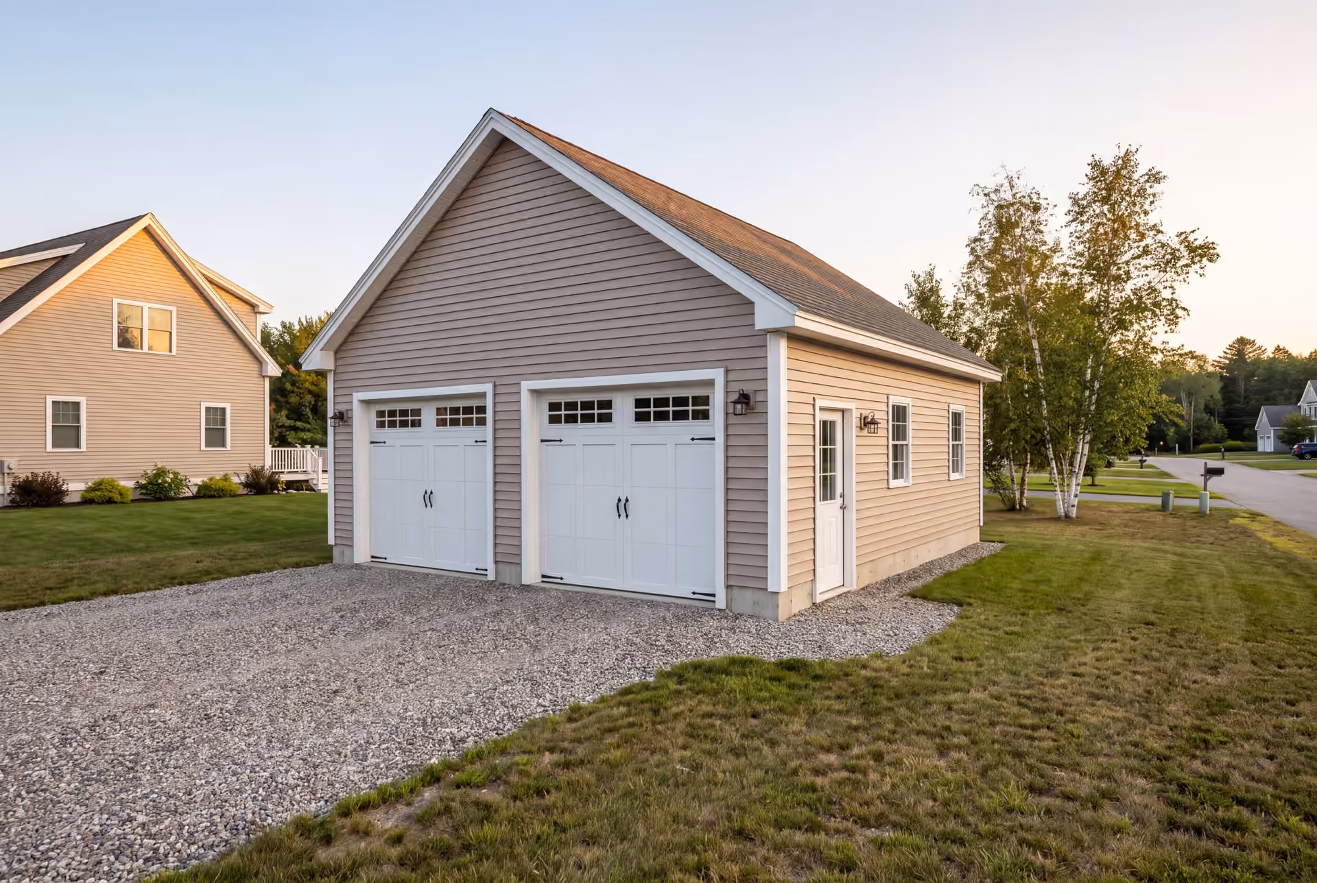 garage builder in Windham, ME: illustrative scene, A newly built, detached two-bay garage with mushroom-colored siding and a gravel driveway
