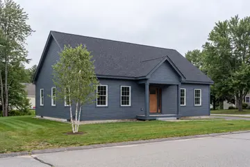 general contractor: illustrative scene, A newly built single-story house with blue siding, a dark roof, and a covered entry, surrounded by green grass and trees