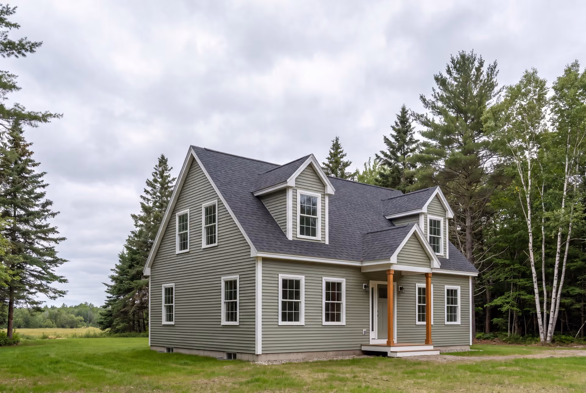 general contractor in Buxton, ME: illustrative scene, A newly built Cape house with sage green siding and a dark roof, set in a grassy area with trees