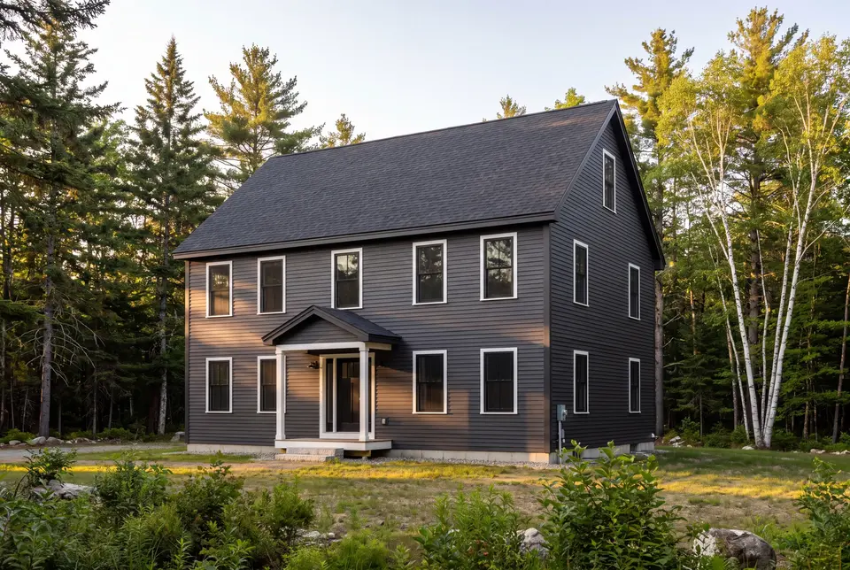 Illustration: A newly built two-story Colonial house with dark gray siding and a dark gray roof, surrounded by trees and natural landscaping