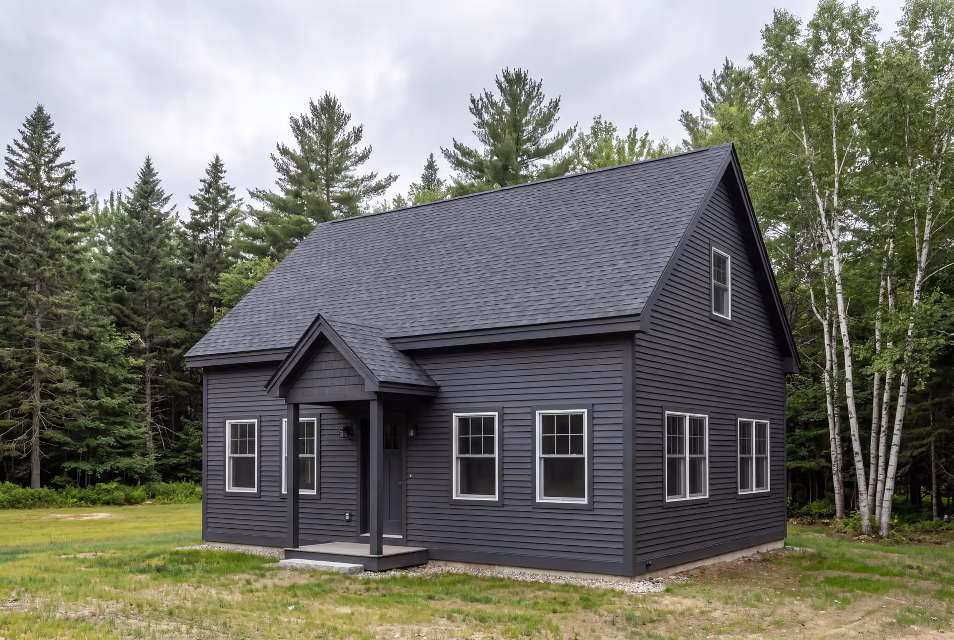 general contractor in Falmouth, ME: illustrative scene, A dark charcoal cottage with white-trimmed windows and a covered entry, set against a backdrop of green trees under a cloudy sky